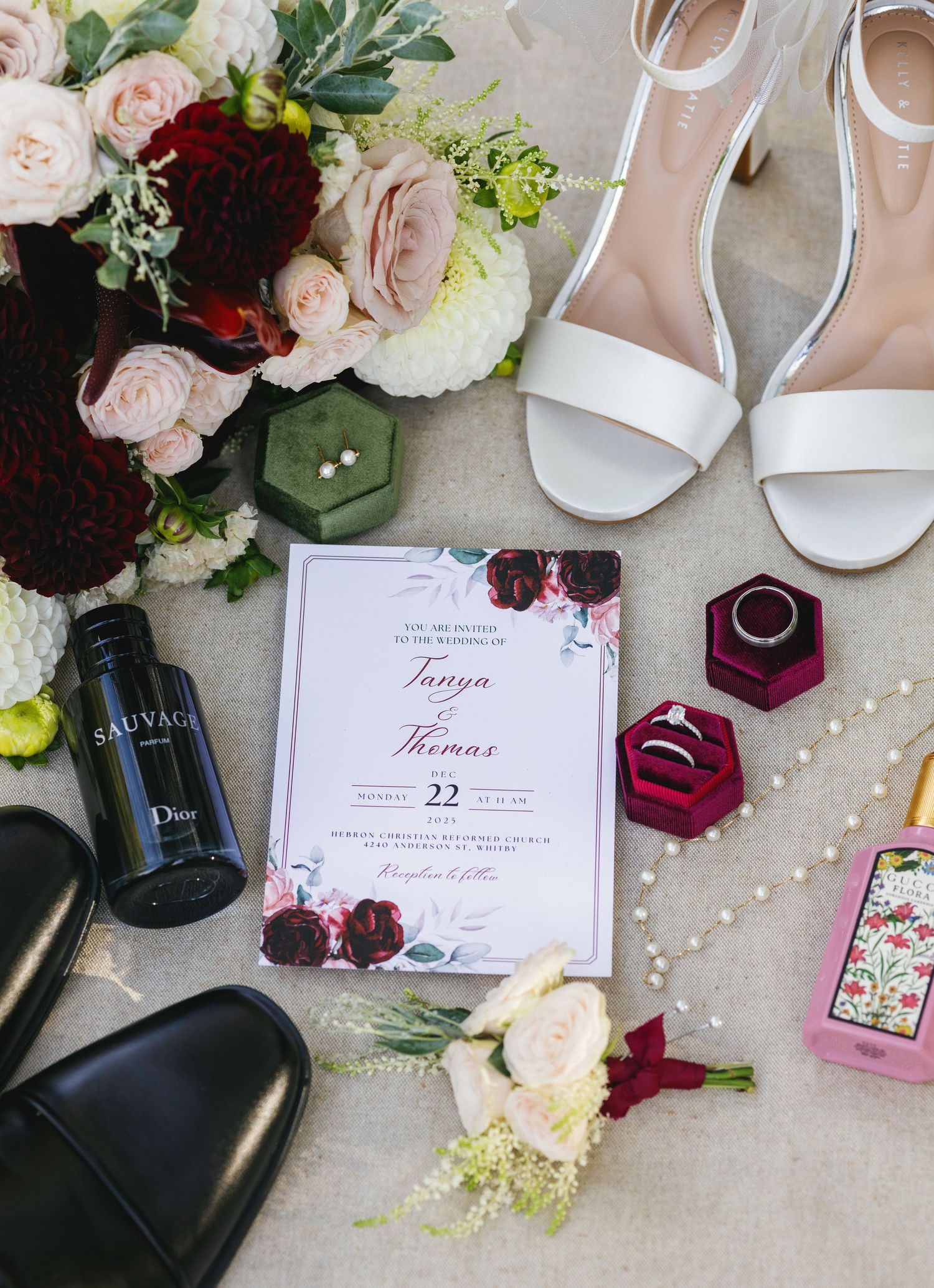 Wedding flat lay with floral invitation for Tanya and Thomas, white heels, rings, Dior cologne, and bridal bouquet.