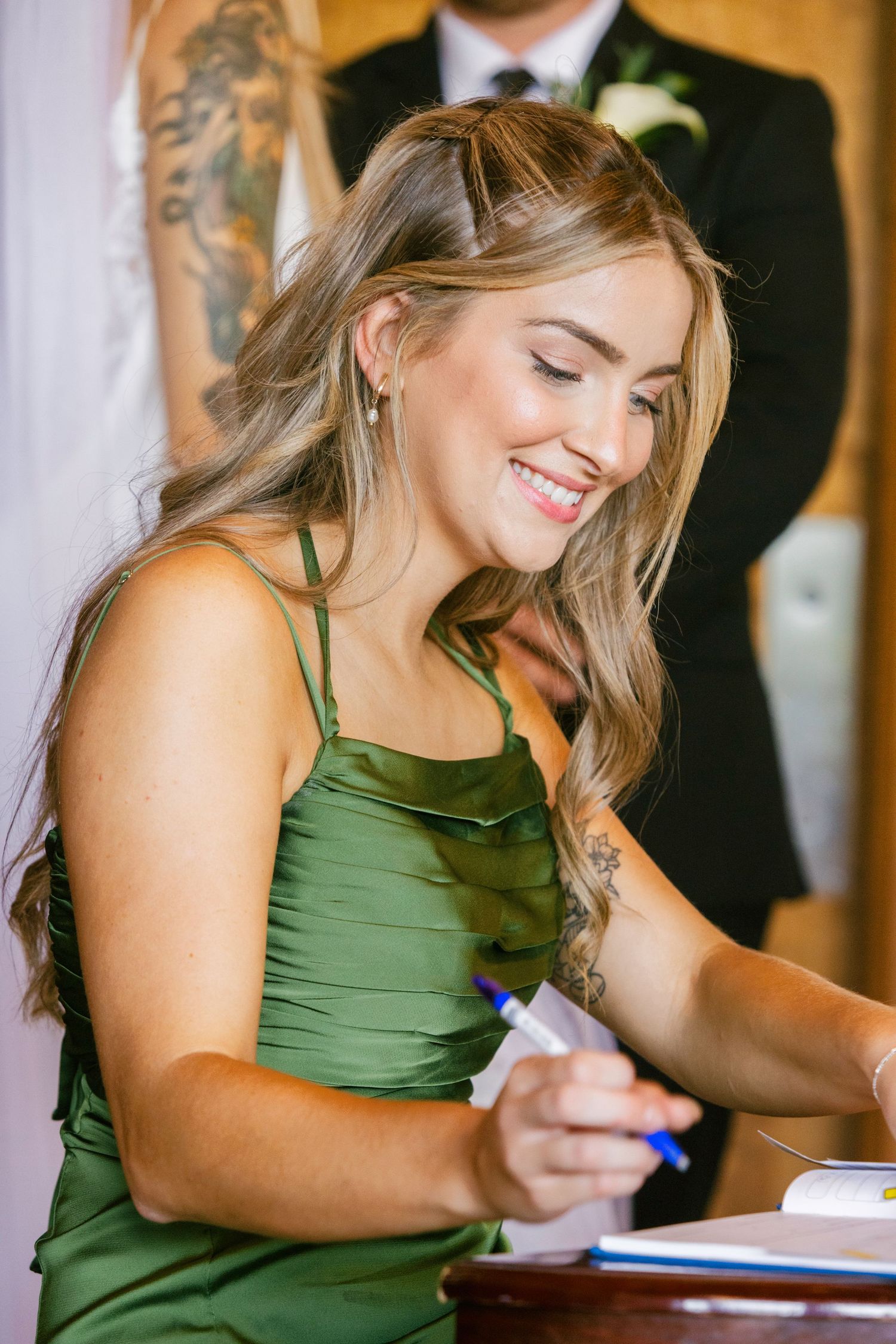 Woman in green sleeveless dress smiles while writing at a table during an event.