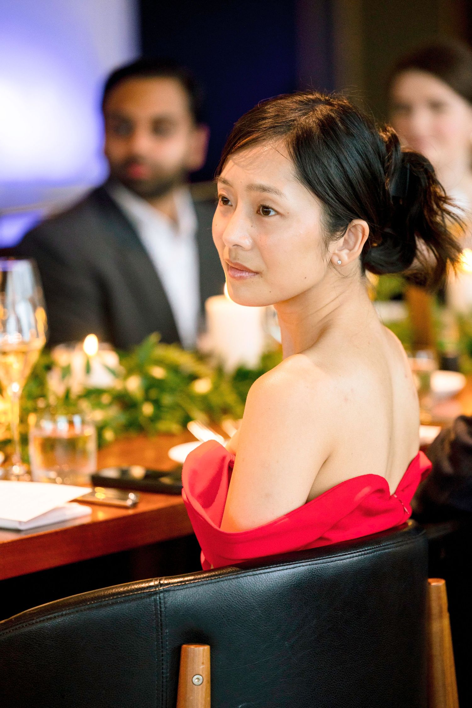 Elegant dining scene with a guest in a red dress seated at a formal table setting.