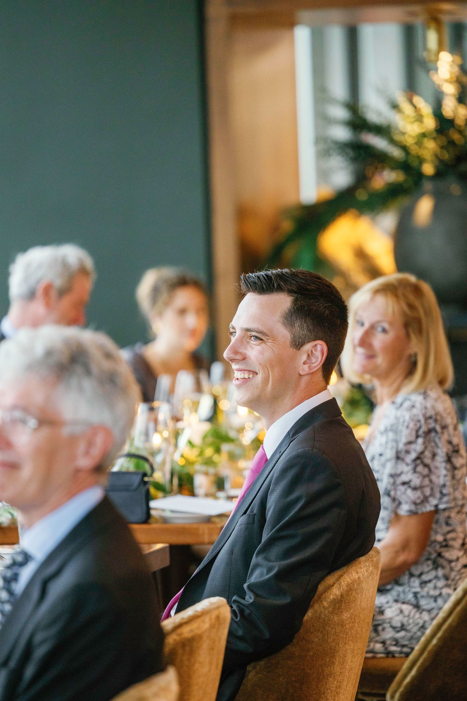 Guests in formal attire seated at an upscale dining event with warm ambient lighting.