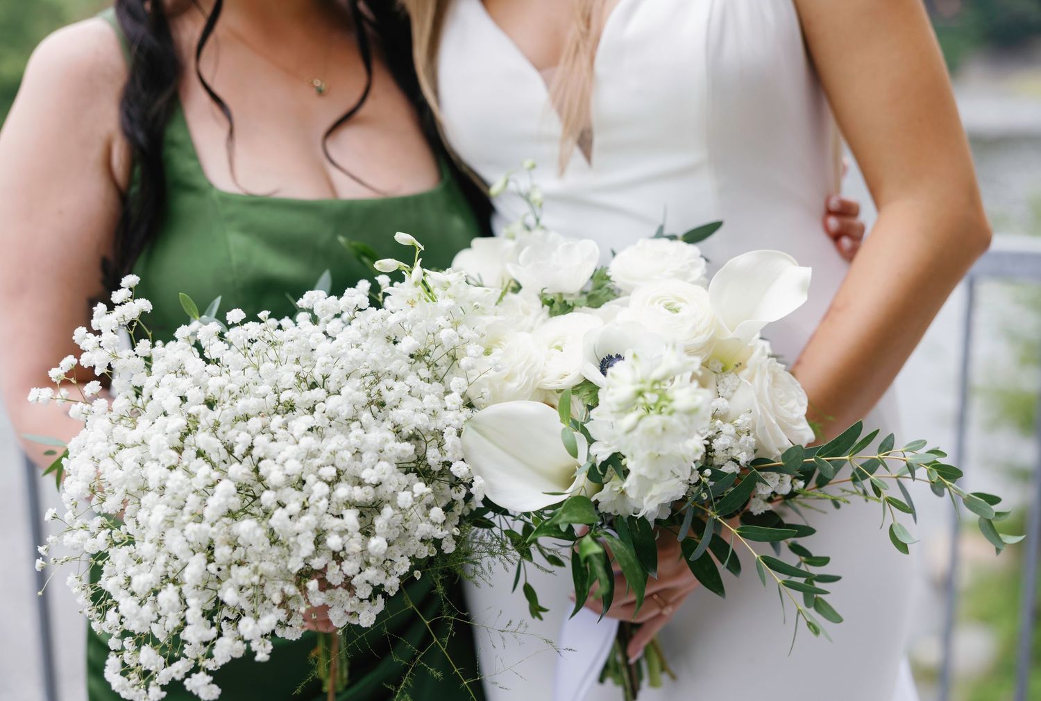 A row of elegant white and cream wedding bouquets held by bridesmaids in sage green dresses at an outdoor ceremony.