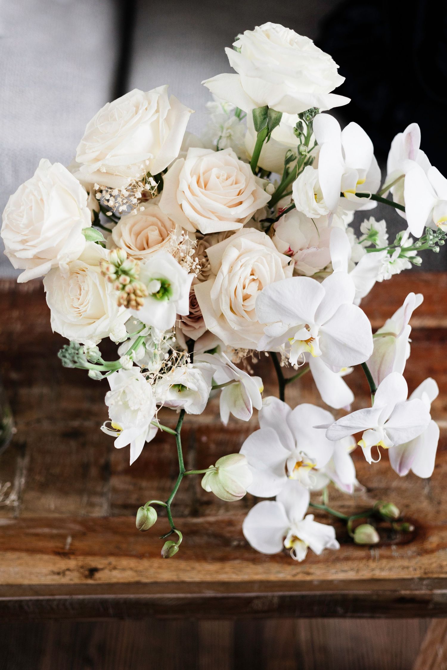 Elegant white and blush floral arrangement with roses and orchids on wooden surface.