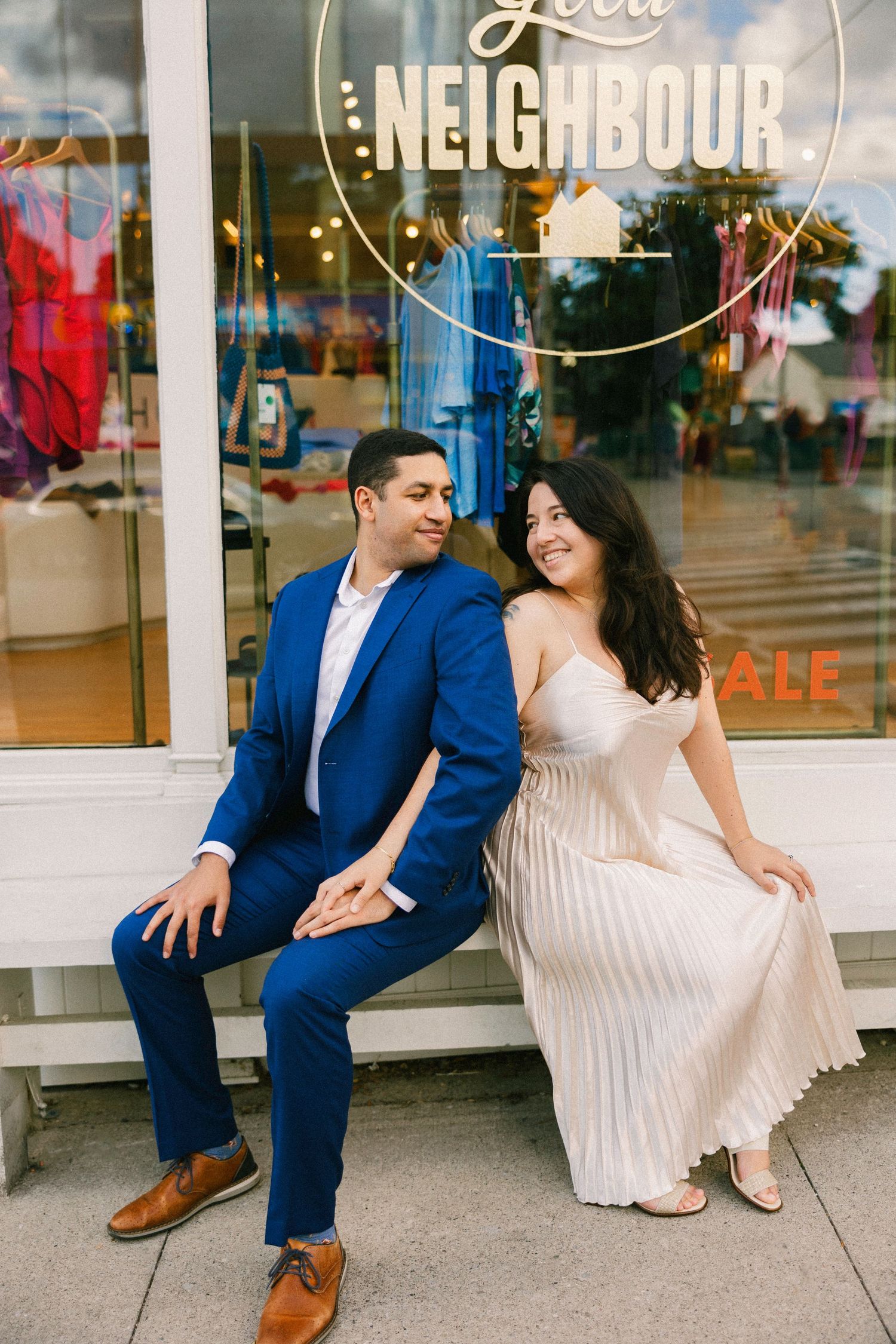 Stylish couple sitting outside storefront with 'Neighbour' sign visible.