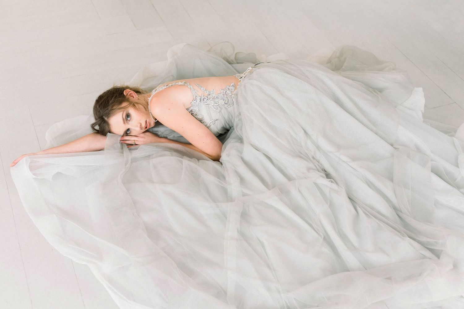 Ethereal boudoir photography featuring woman in white dress on light bedding.