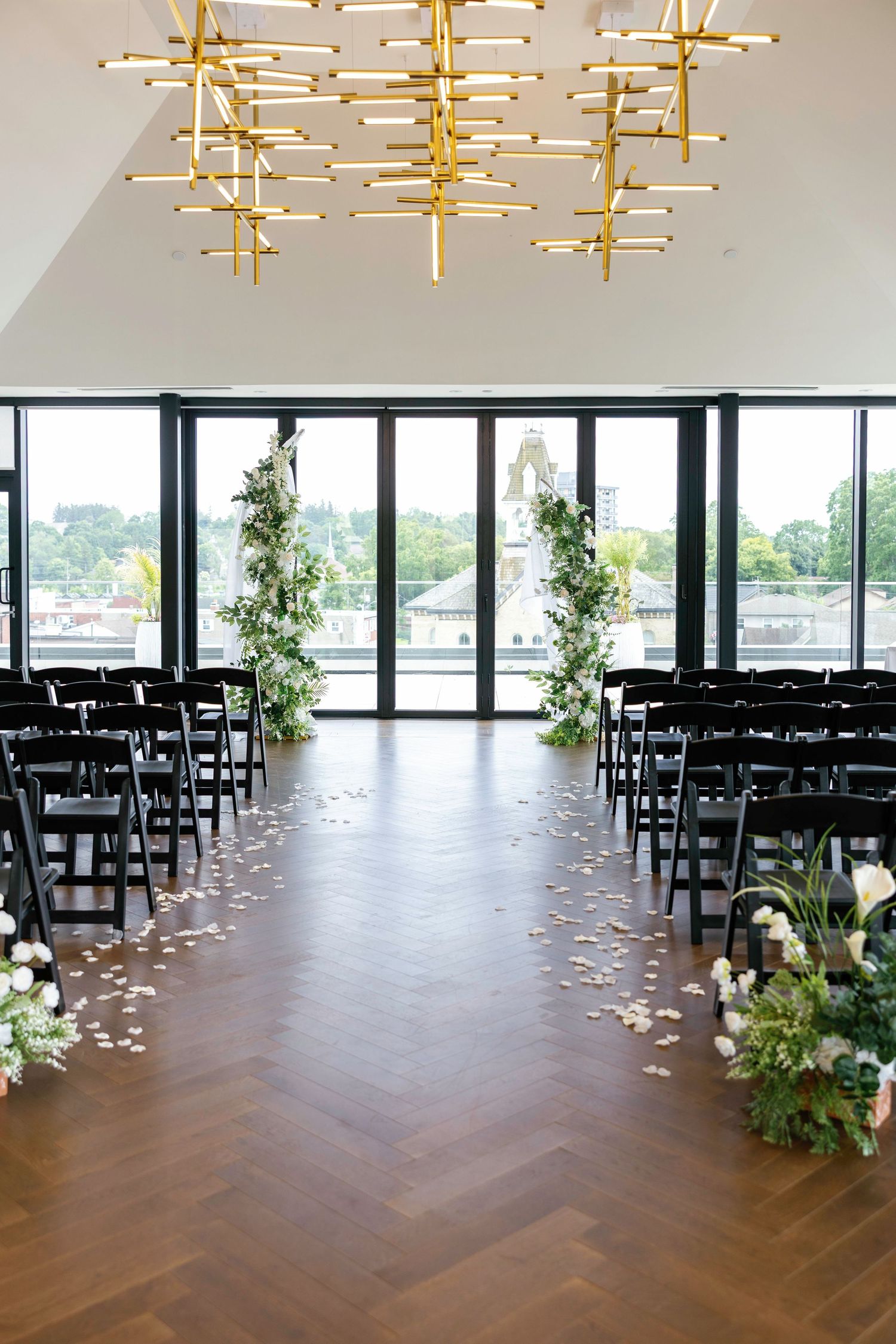 Modern wedding ceremony space with gold geometric chandeliers and black chairs in herringbone floor pattern.