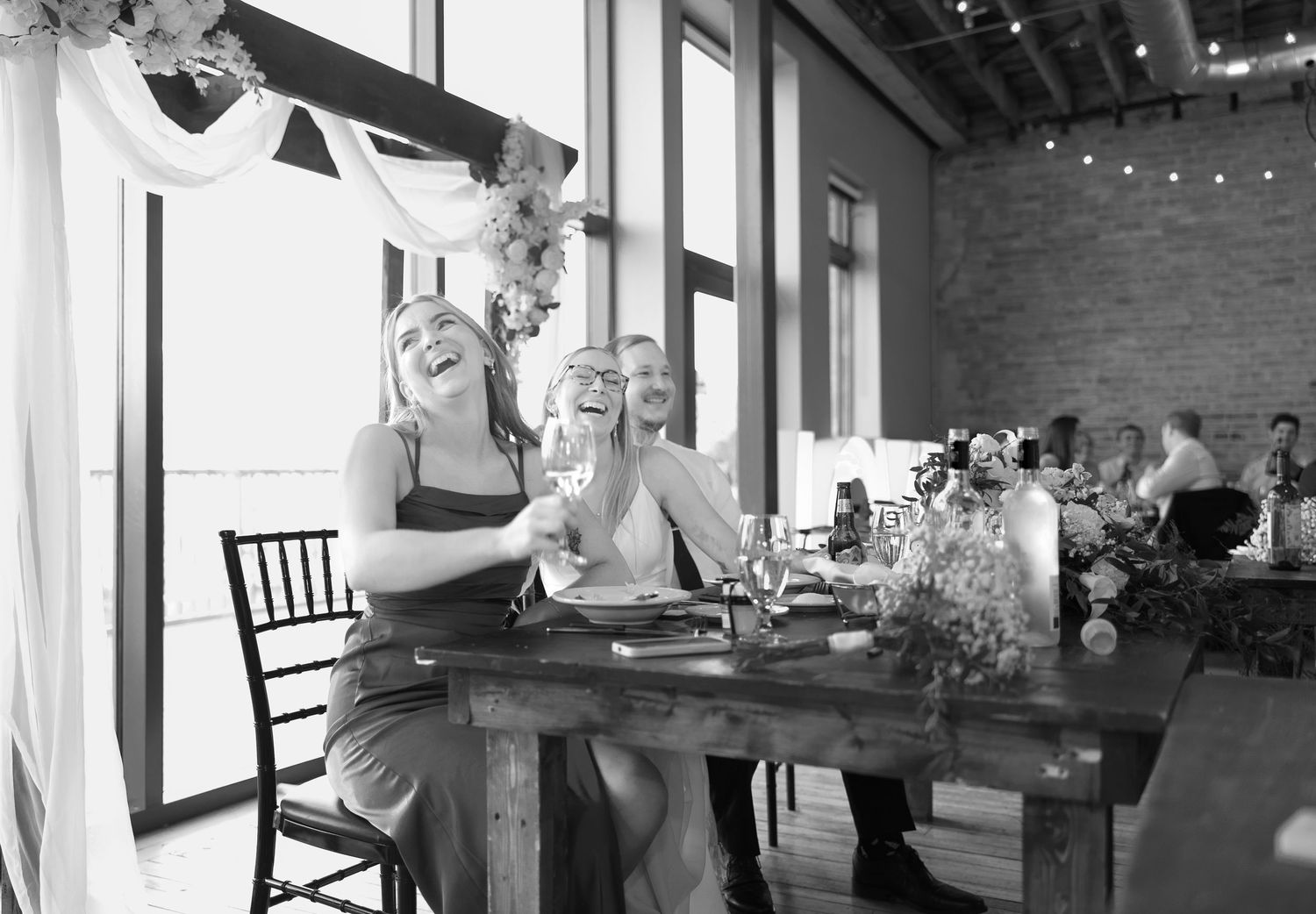 Restaurant diners enjoying meals and conversation in a cozy brick-walled dining room with string lights overhead.