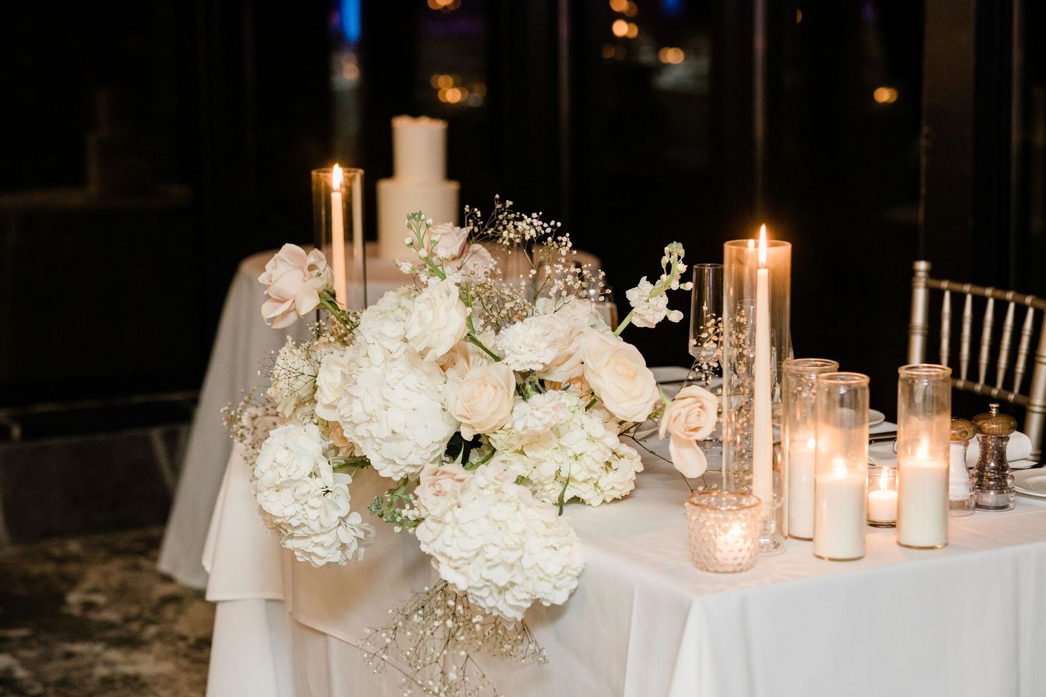 Elegant wedding reception table with white floral centerpiece and glowing candles at night.