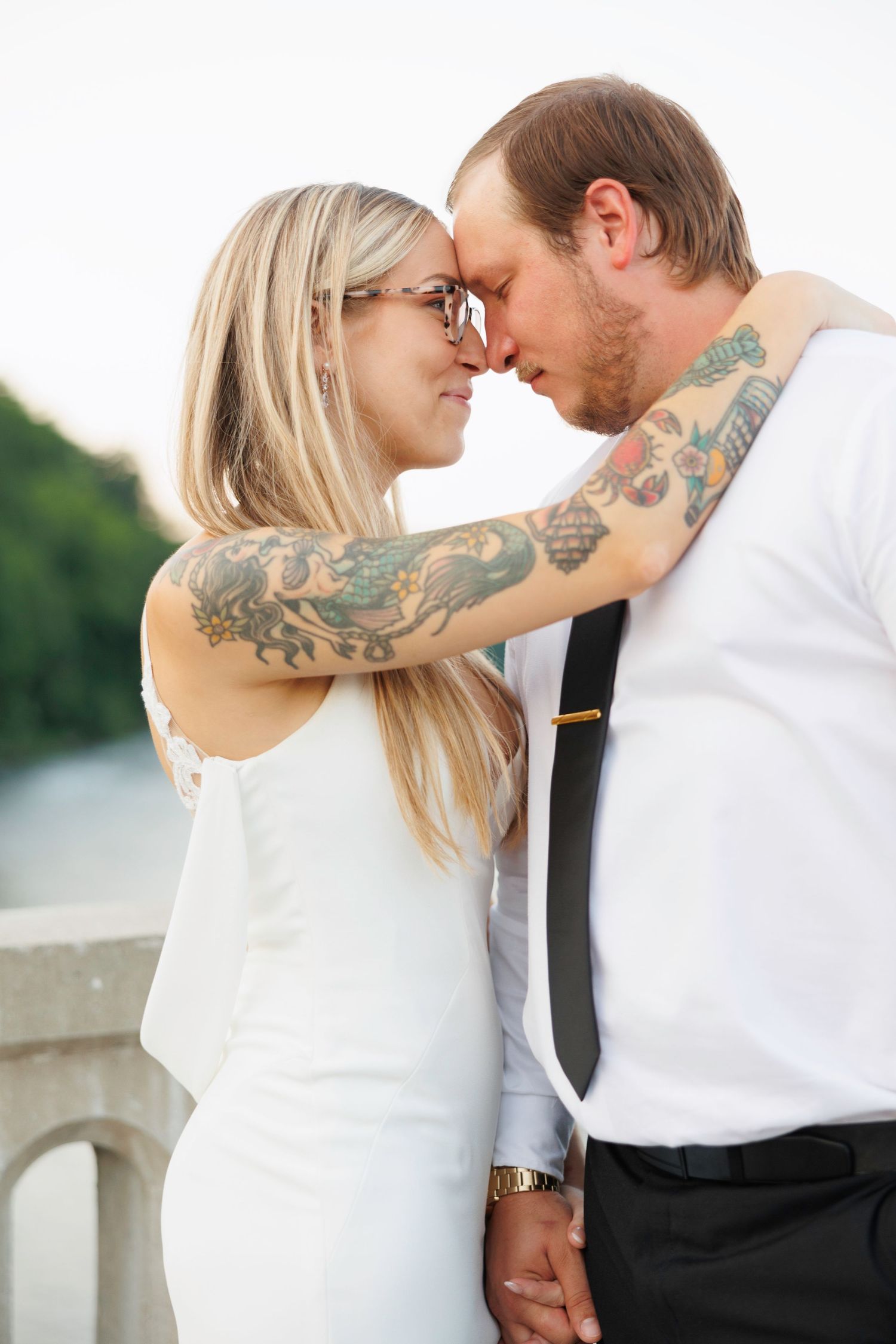 A couple in white and black attire sharing tender moments against a bright outdoor backdrop.