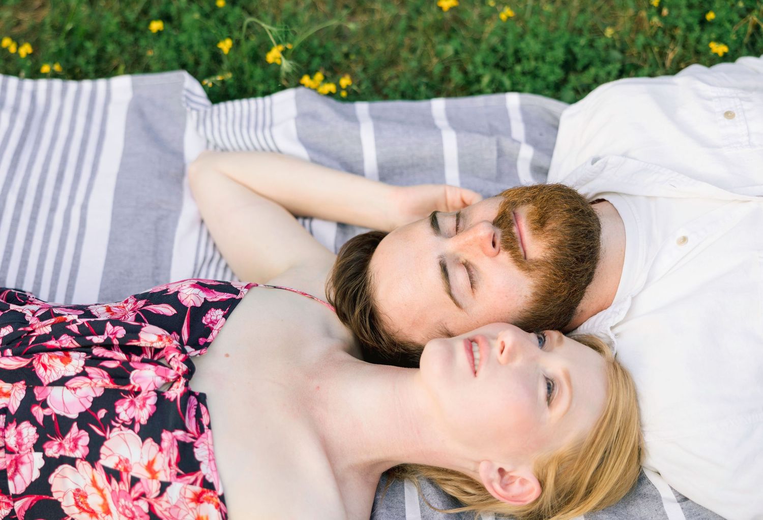 Couple lying on white blanket outdoors surrounded by yellow wildflowers.