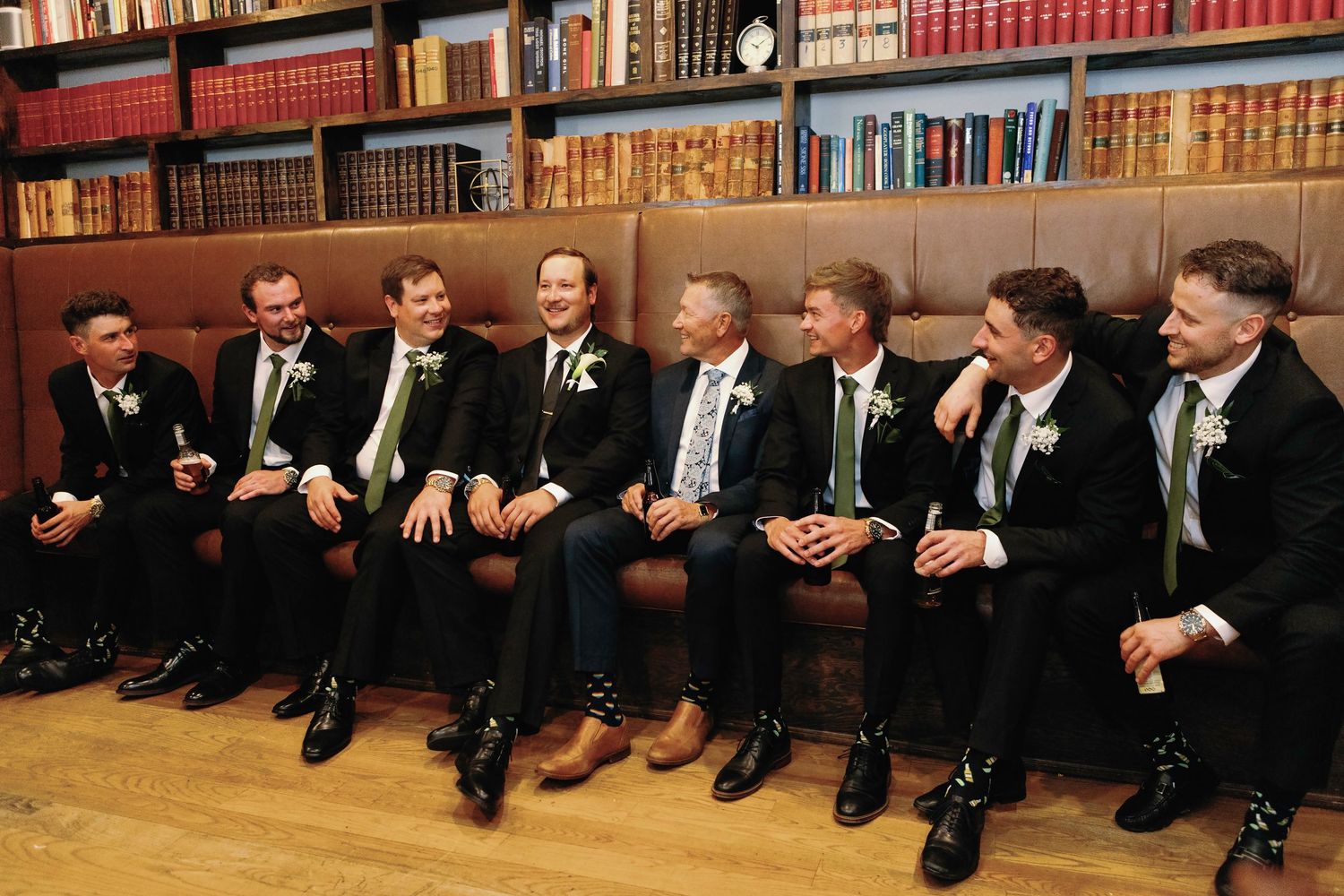 Row of people sitting on floor against bookshelf showing only their legs and dress shoes in formal attire.