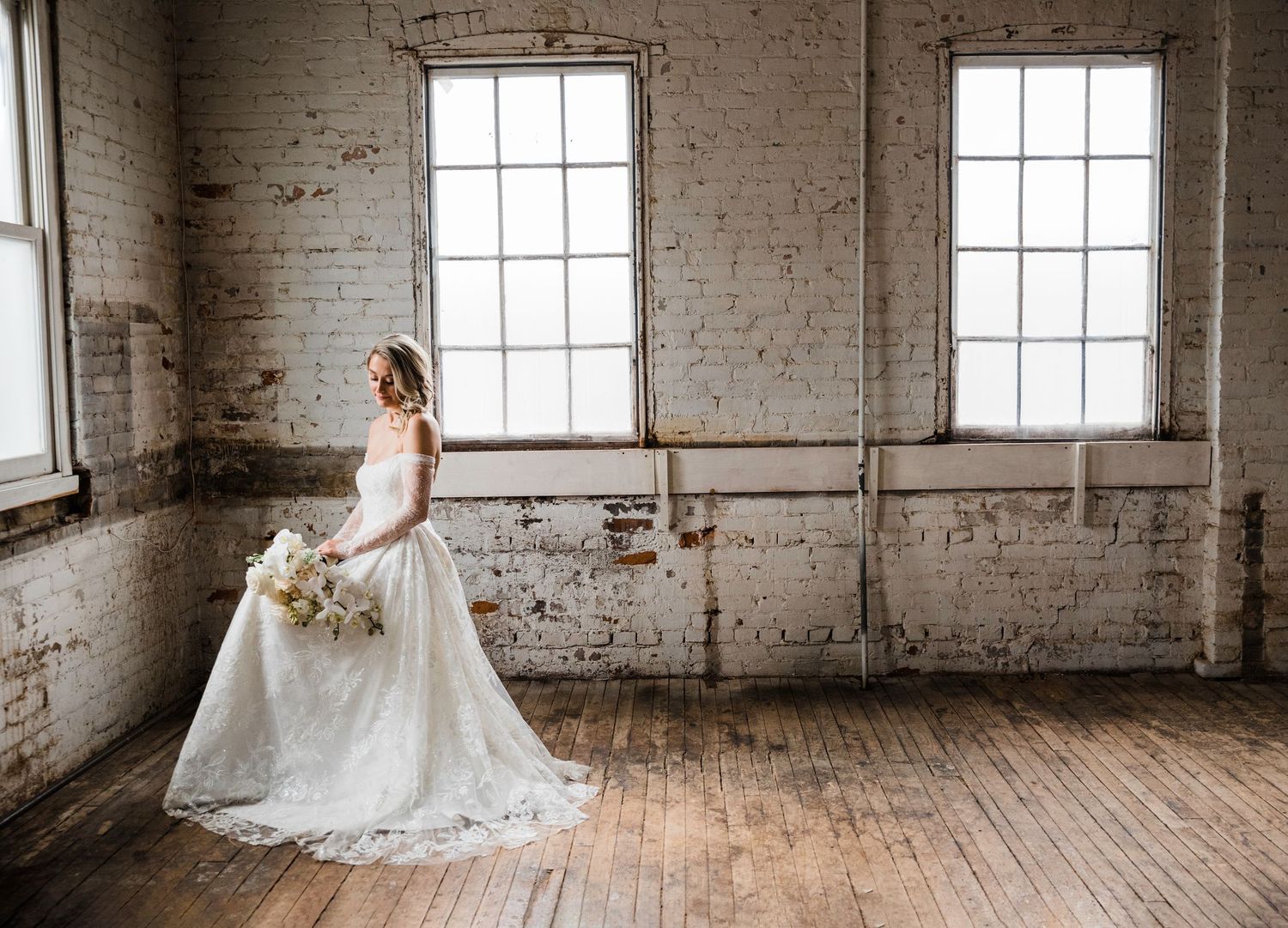 Sunlit wedding venue features rustic wooden floors and exposed brick walls with large windows.