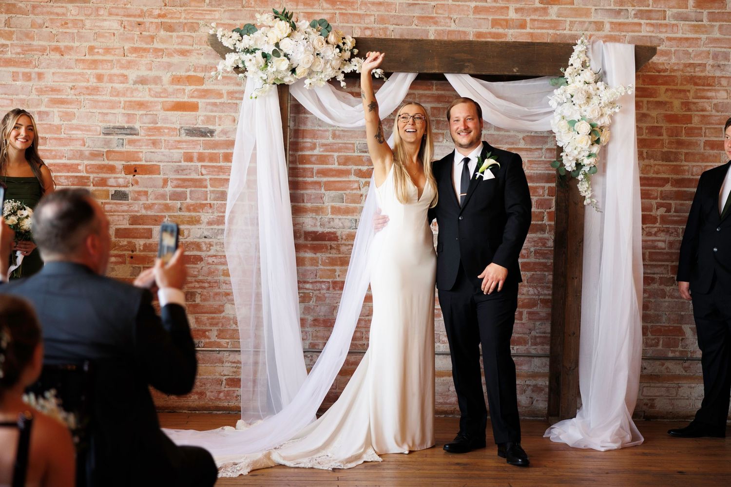 Wedding ceremony setup in an industrial venue with exposed brick walls and white fabric draping creating an elegant aisle.