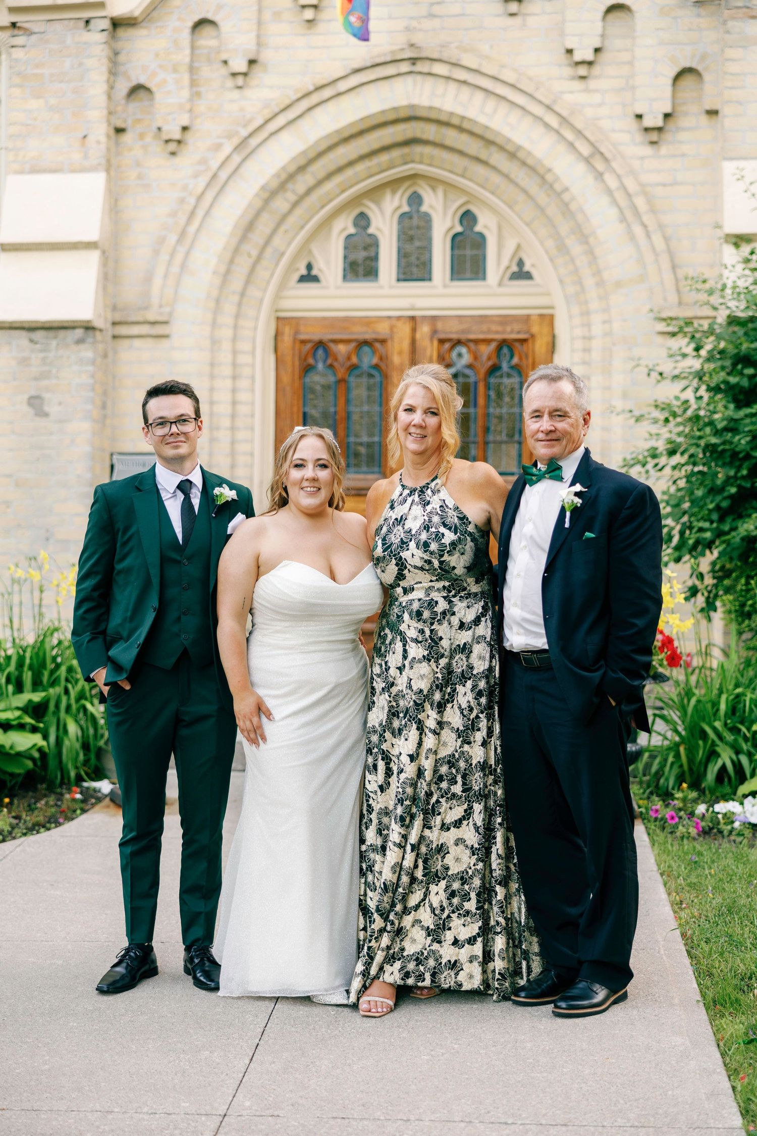 Wedding party poses outside a grand stone church with Gothic architecture.