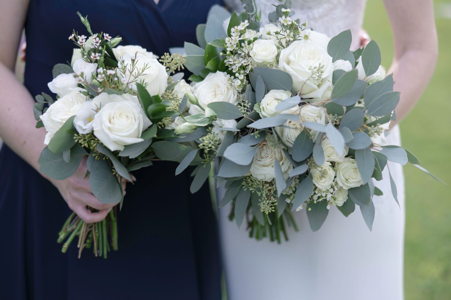 A row of elegant white and green wedding bouquets held by people wearing navy and white formal attire.