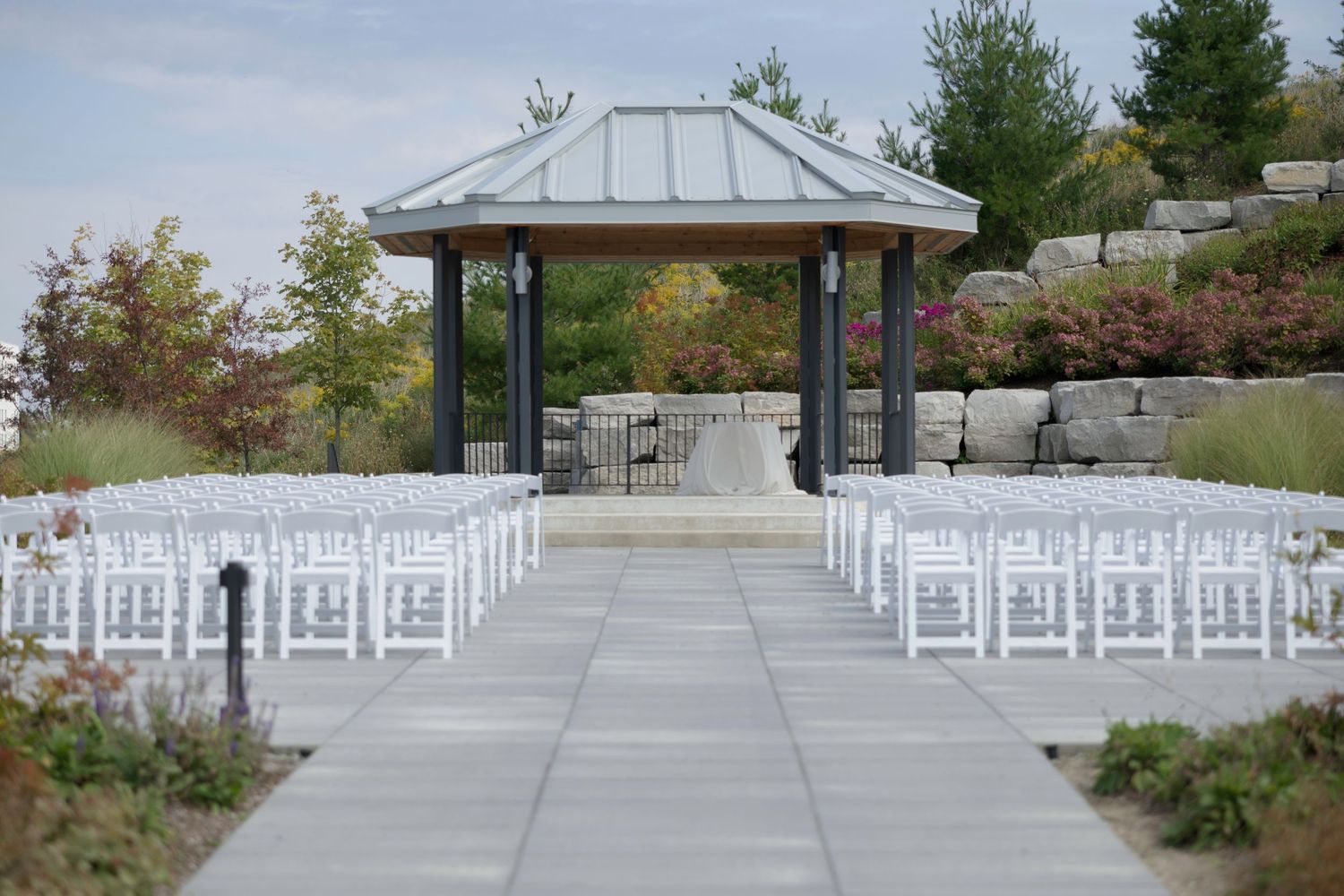 White chairs arranged in rows for an outdoor wedding ceremony with a modern gazebo and scenic landscaping in the background.