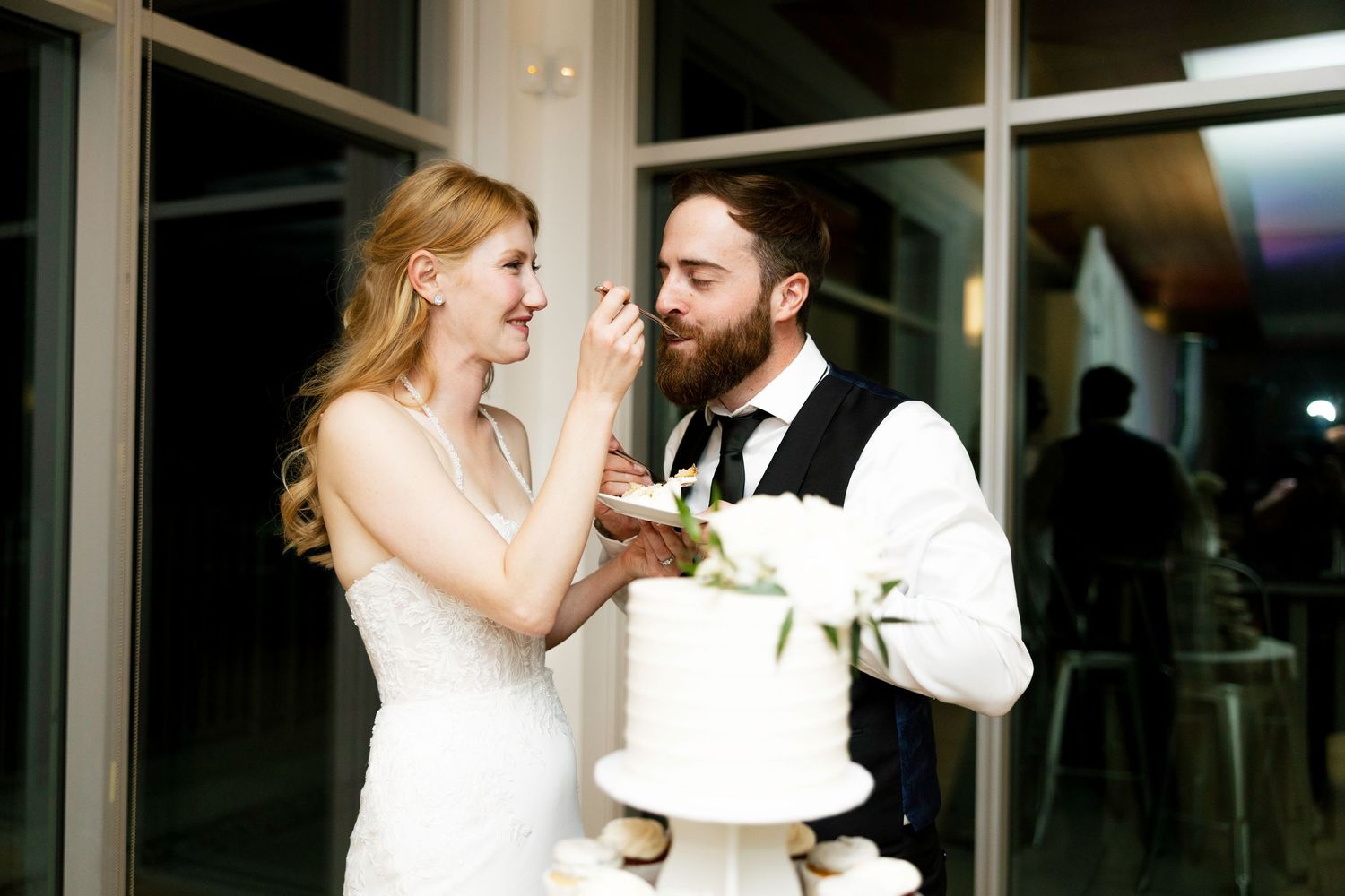 A bride and groom share a joyful moment while cutting their wedding cake together at their reception.