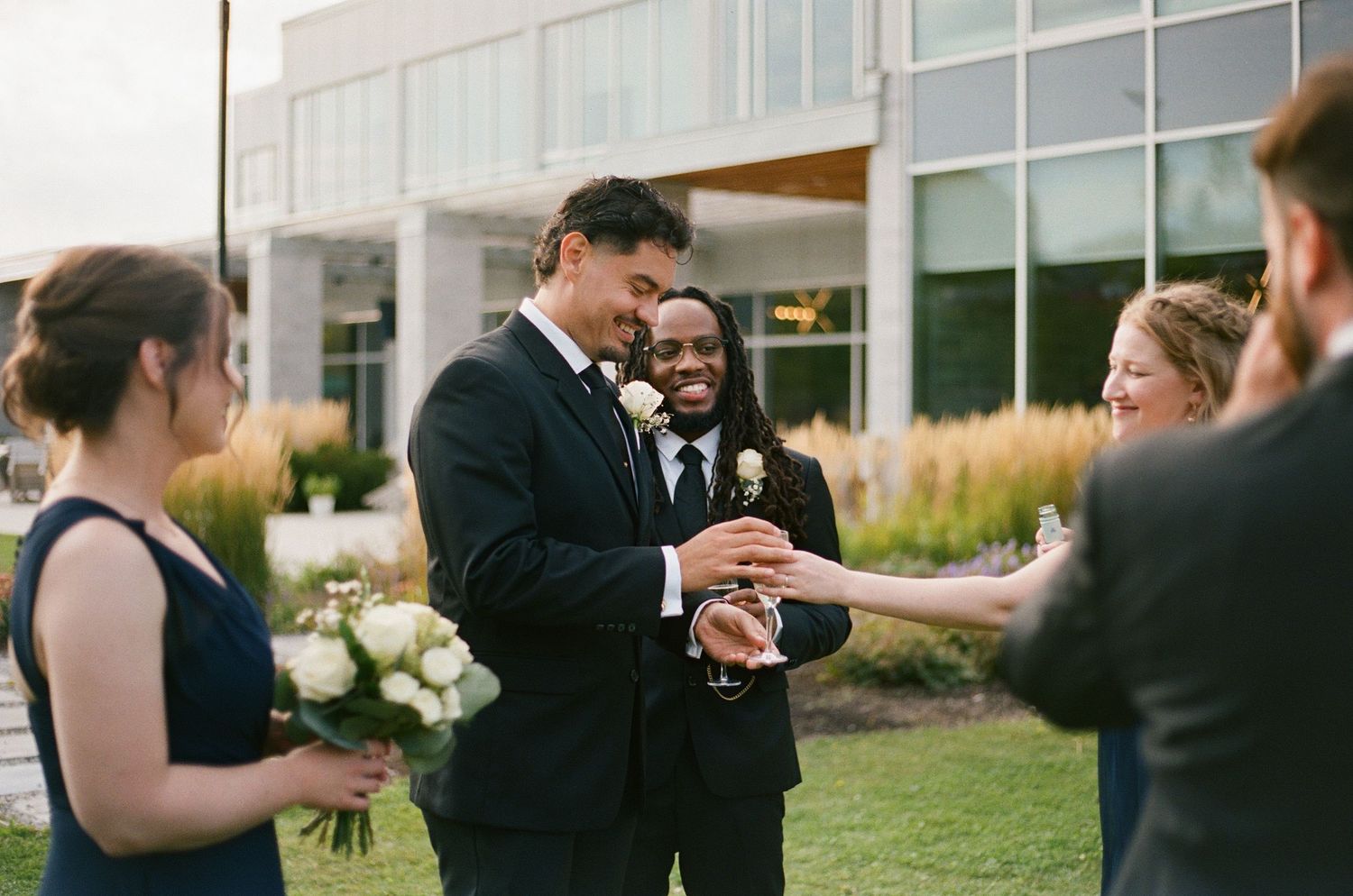 Wedding guests enjoy cocktail hour on a patio while mingling and taking photos in formal attire.