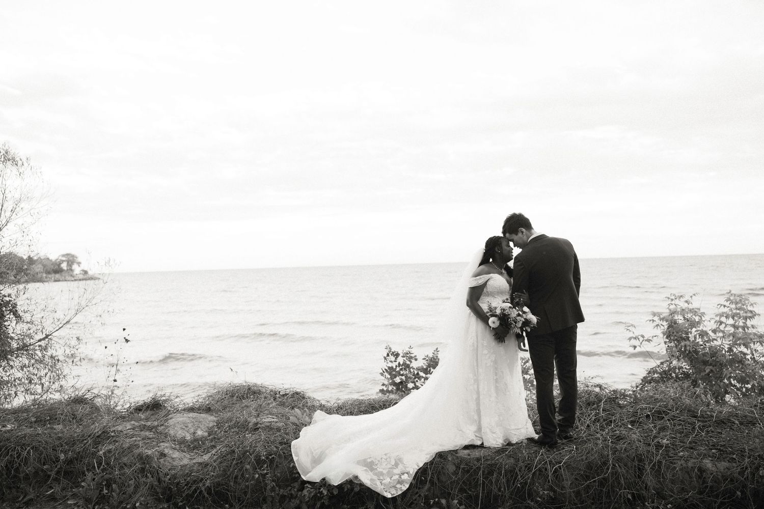 Black and white wedding photos showing romantic moments by the ocean at sunset.