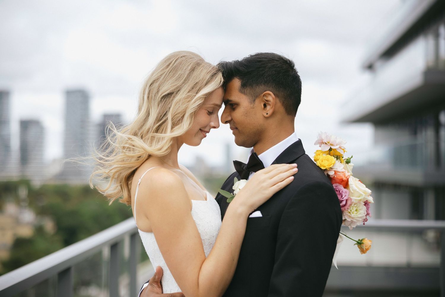 Bride and groom share a romantic moment on a rooftop balcony with city skyline backdrop on their wedding day.