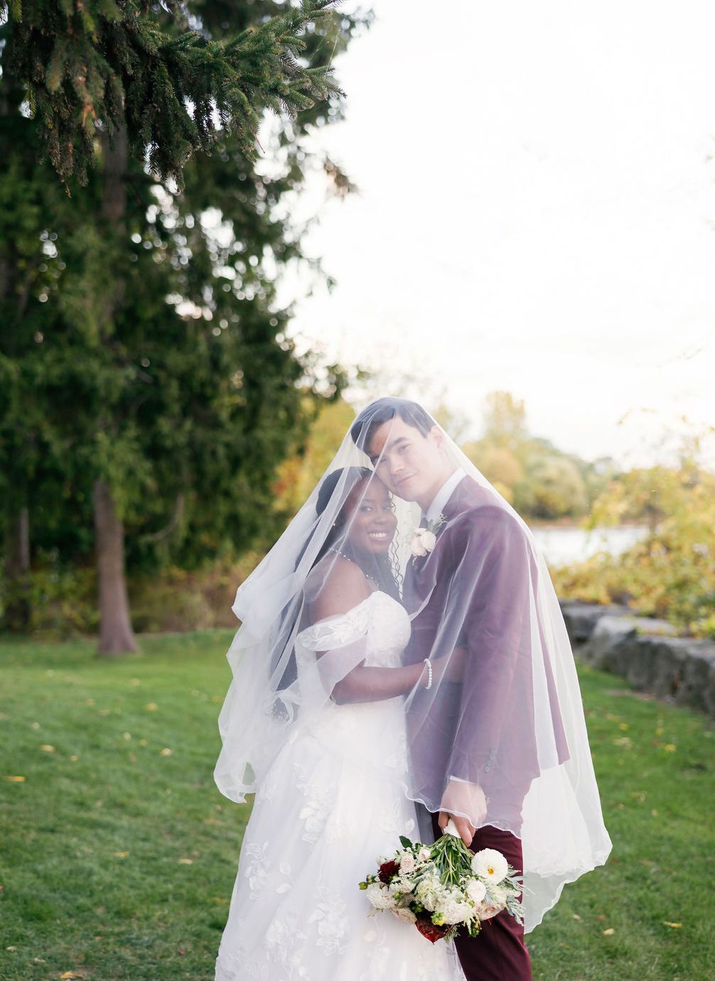 Romantic wedding portraits under a flowing veil in a garden setting at sunset.