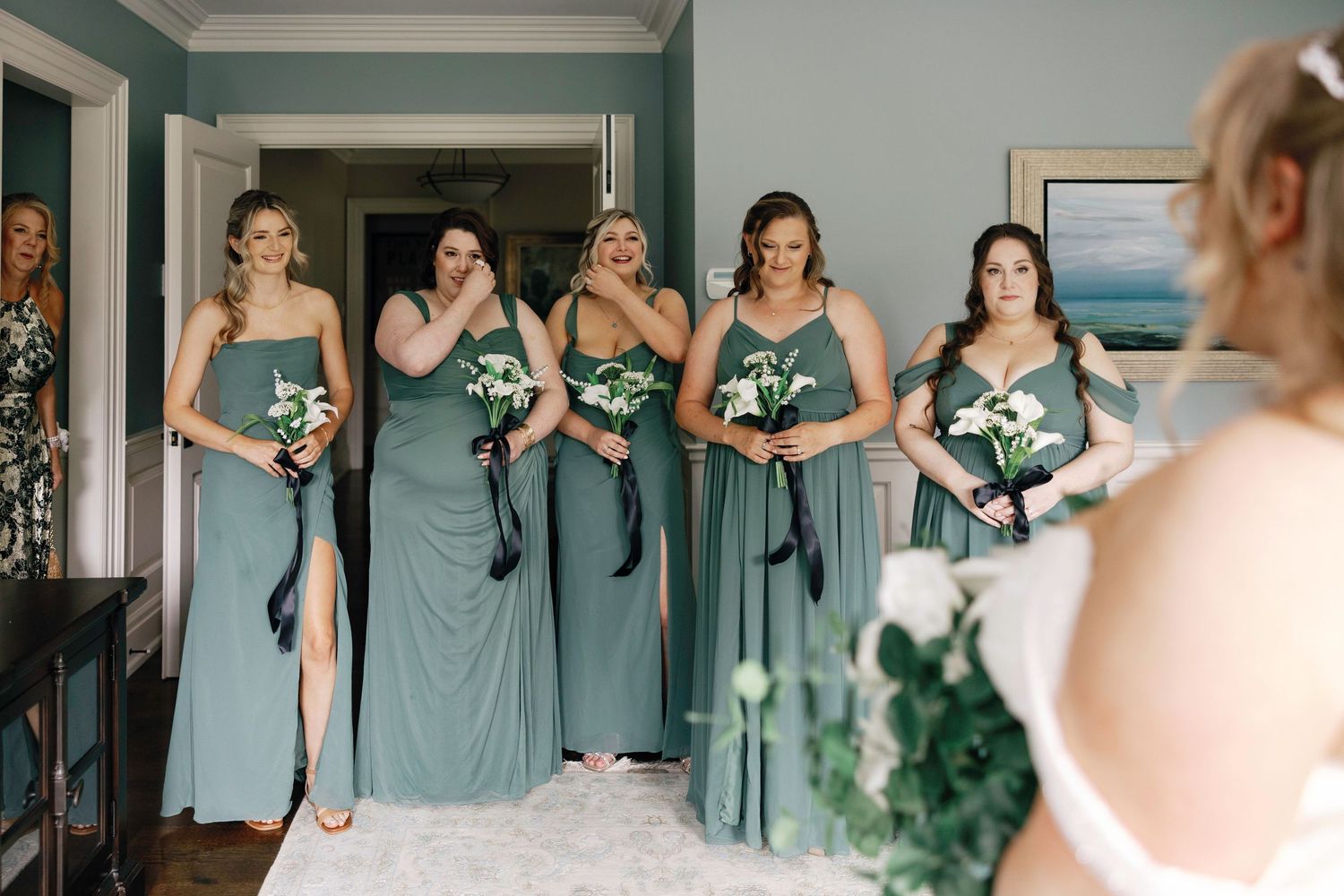 Bridesmaids in sage green dresses share joyful moments while getting ready for a wedding celebration.