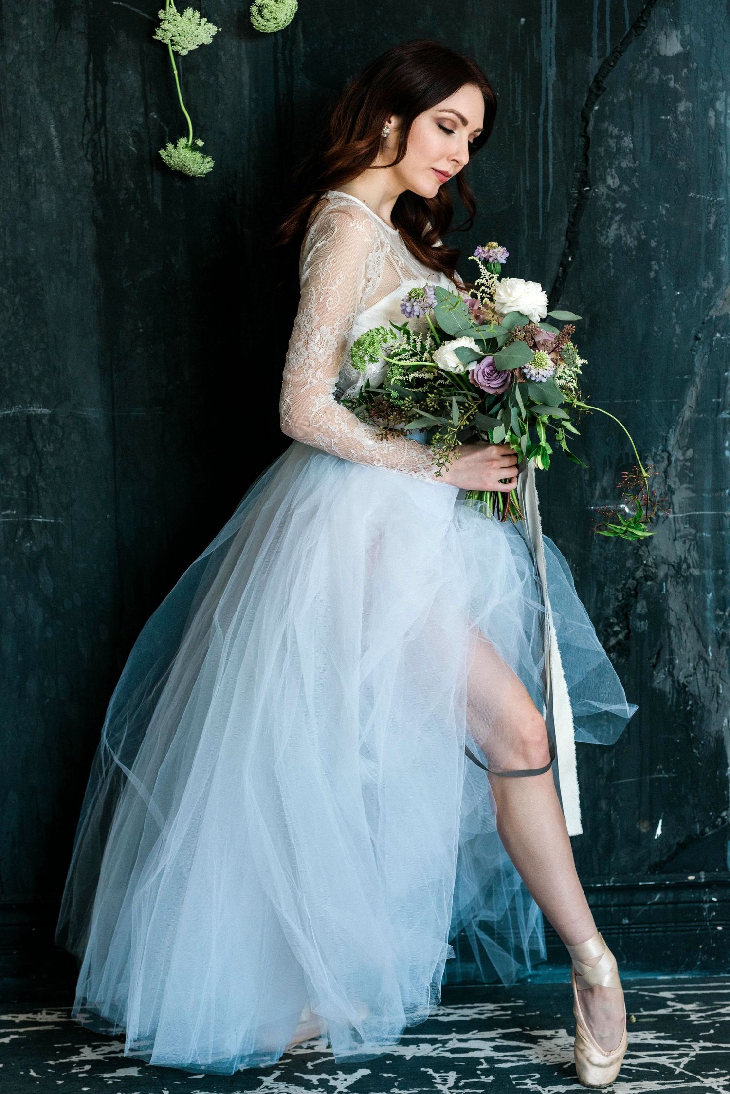 Ethereal bridal portrait featuring a light blue tulle gown and lace bodice with a romantic floral bouquet against dark backdrop.
