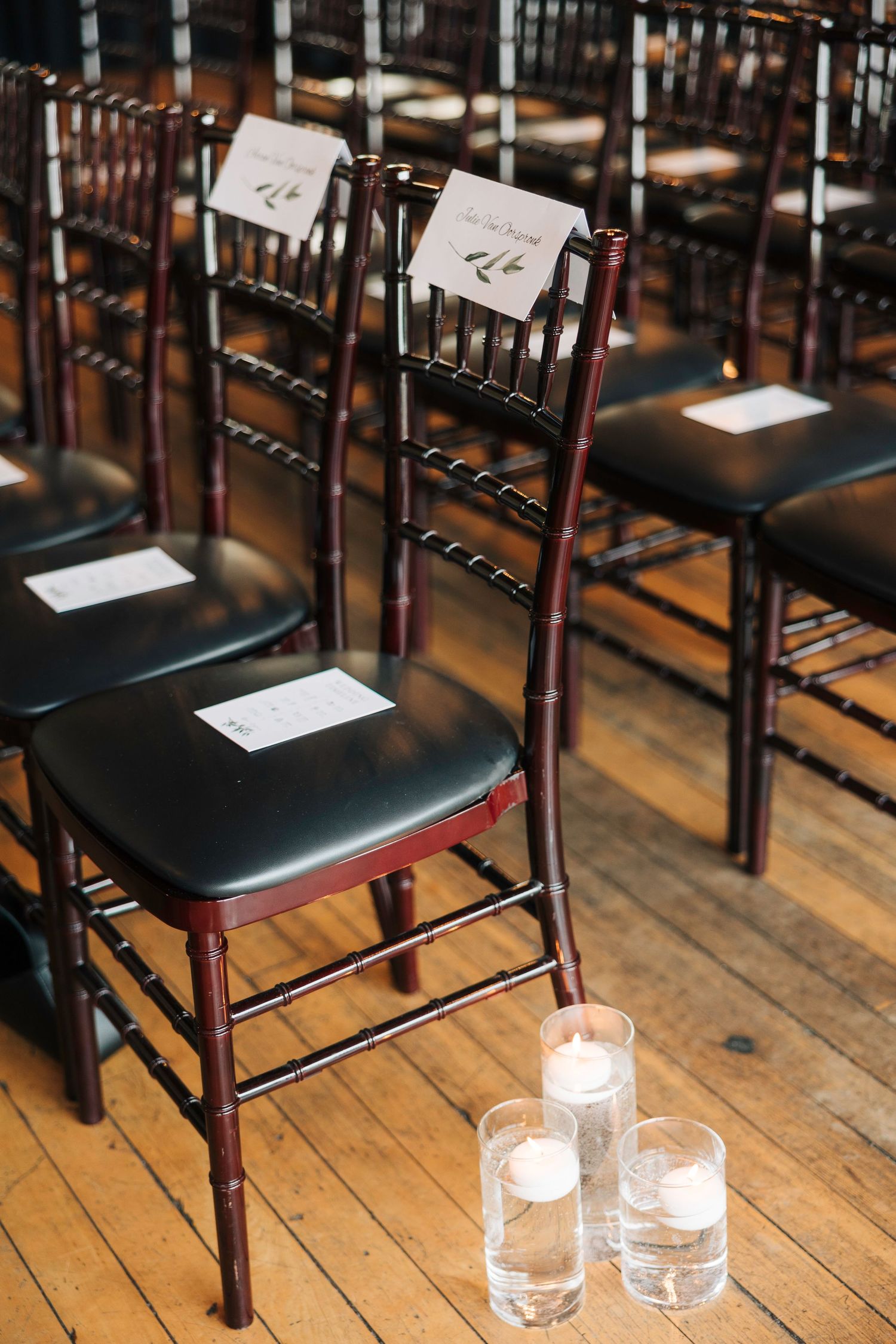 Elegant wedding ceremony setup with mahogany Chiavari chairs and glowing candle votives on rustic wooden floor.