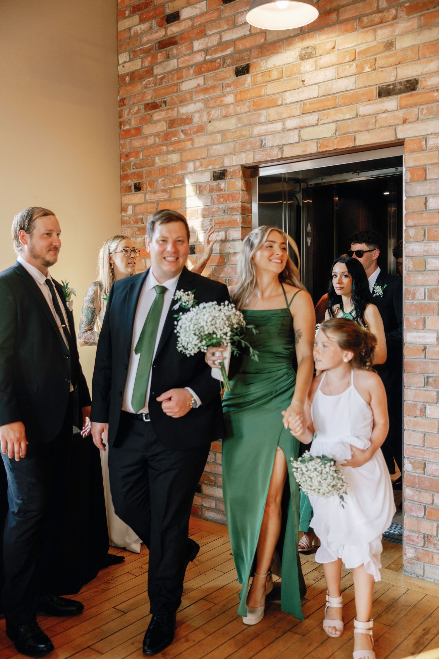 Wedding party in black suits and green dresses celebrating in sequence of candid shots against brick wall.