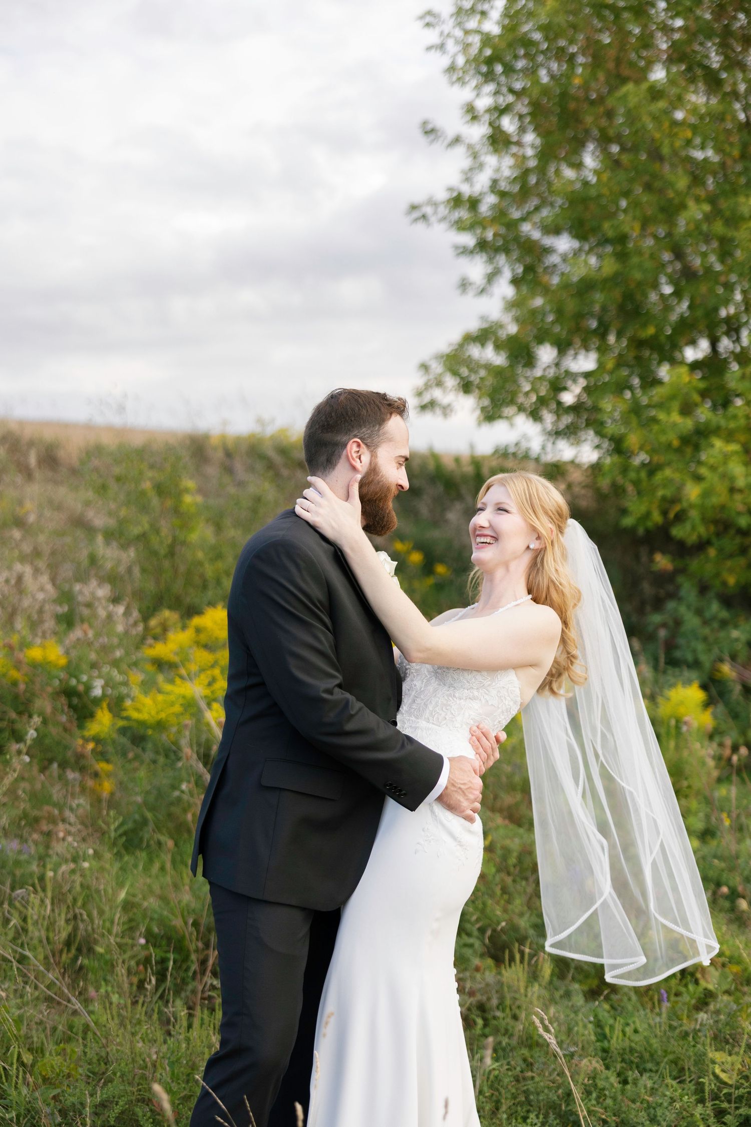 Wedding couple embraces joyfully in an outdoor setting with trees and natural landscape in the background.
