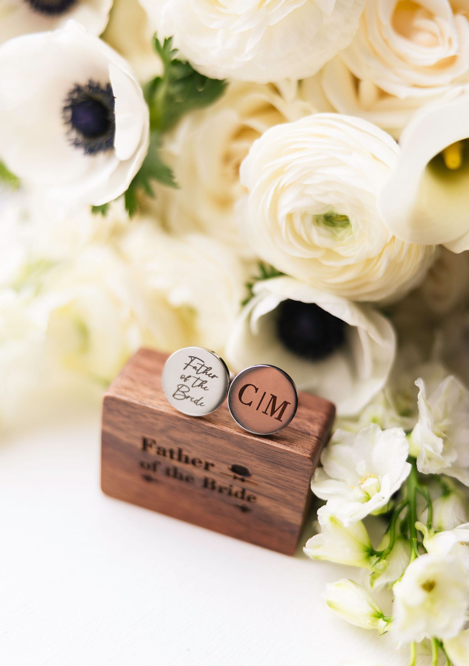 Wooden USB drive with custom engraving surrounded by delicate white ranunculus flowers and greenery.