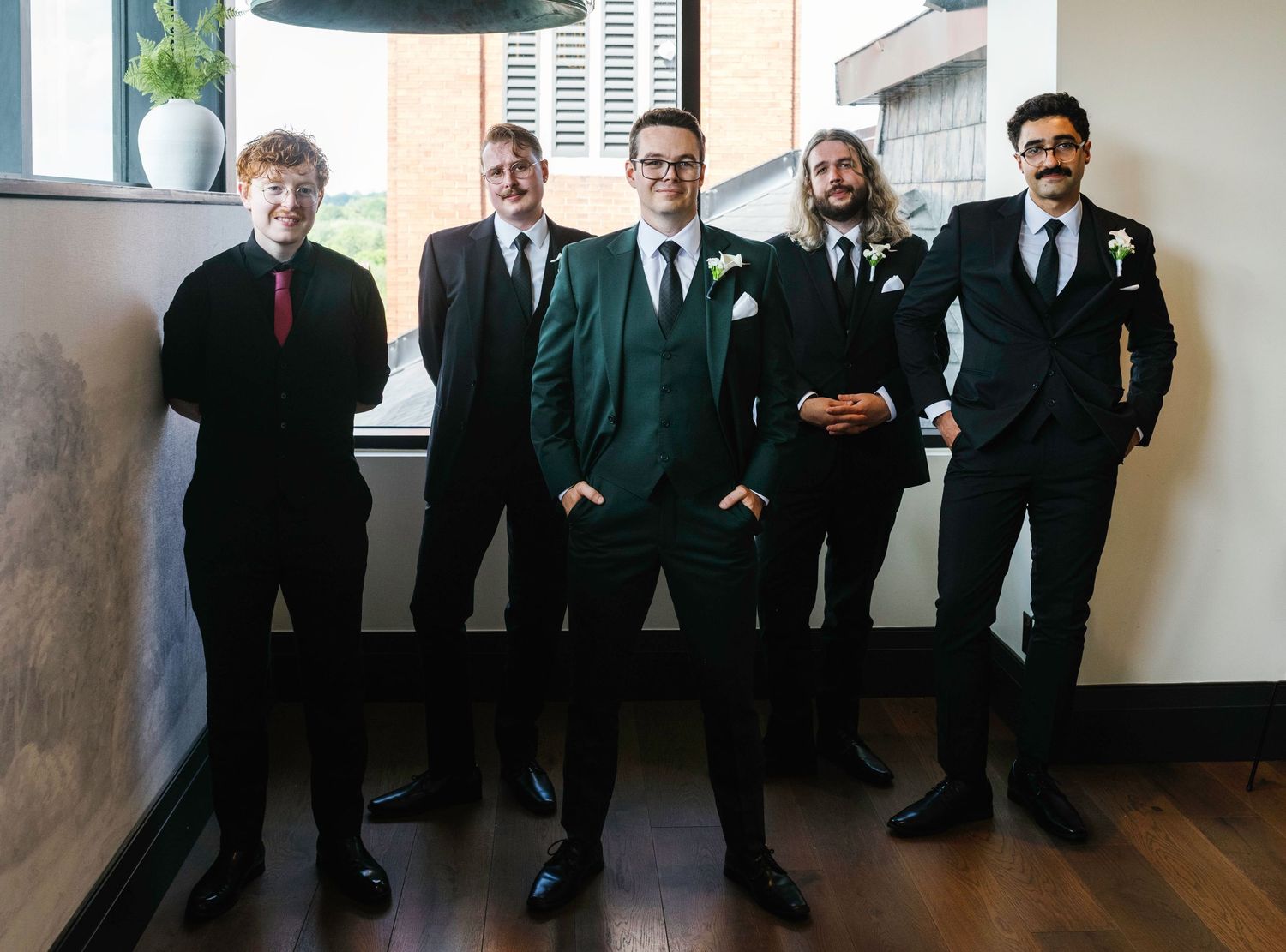 Groomsmen in formal attire pose together, with one wearing a dark green suit as centerpiece.