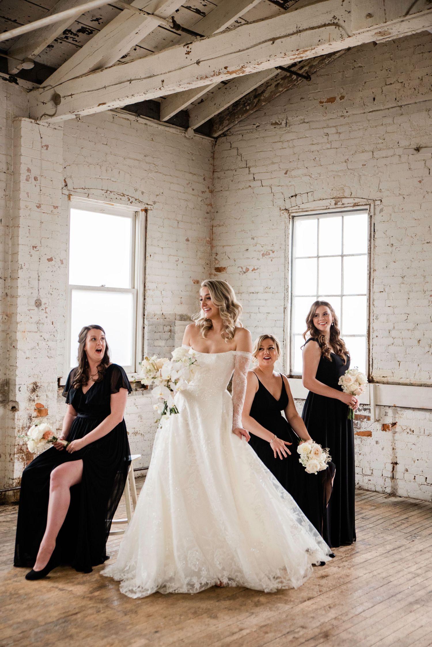 Wedding party poses creatively in rustic white brick venue with natural lighting.