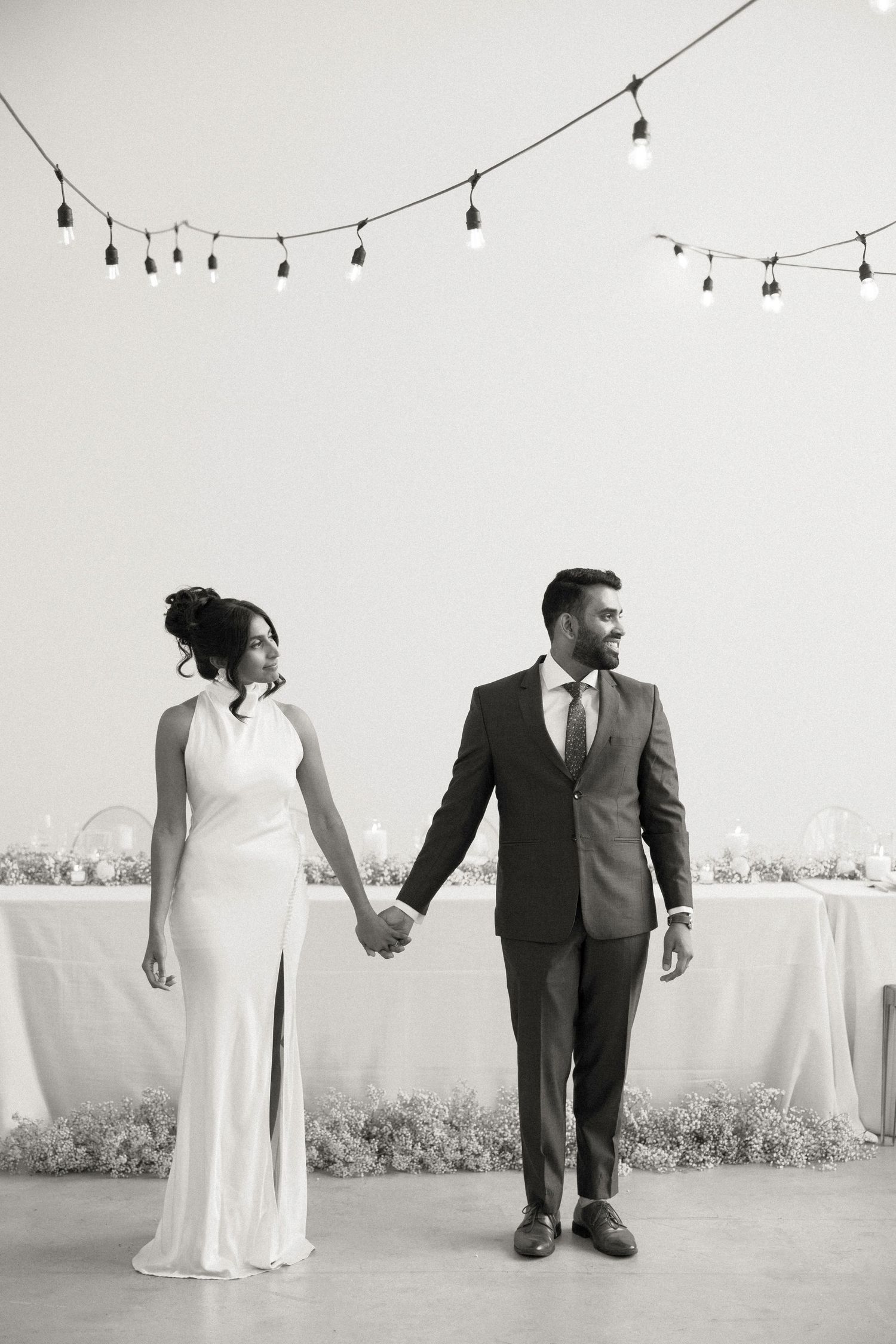Artistic black and white wedding portrait with string lights overhead.