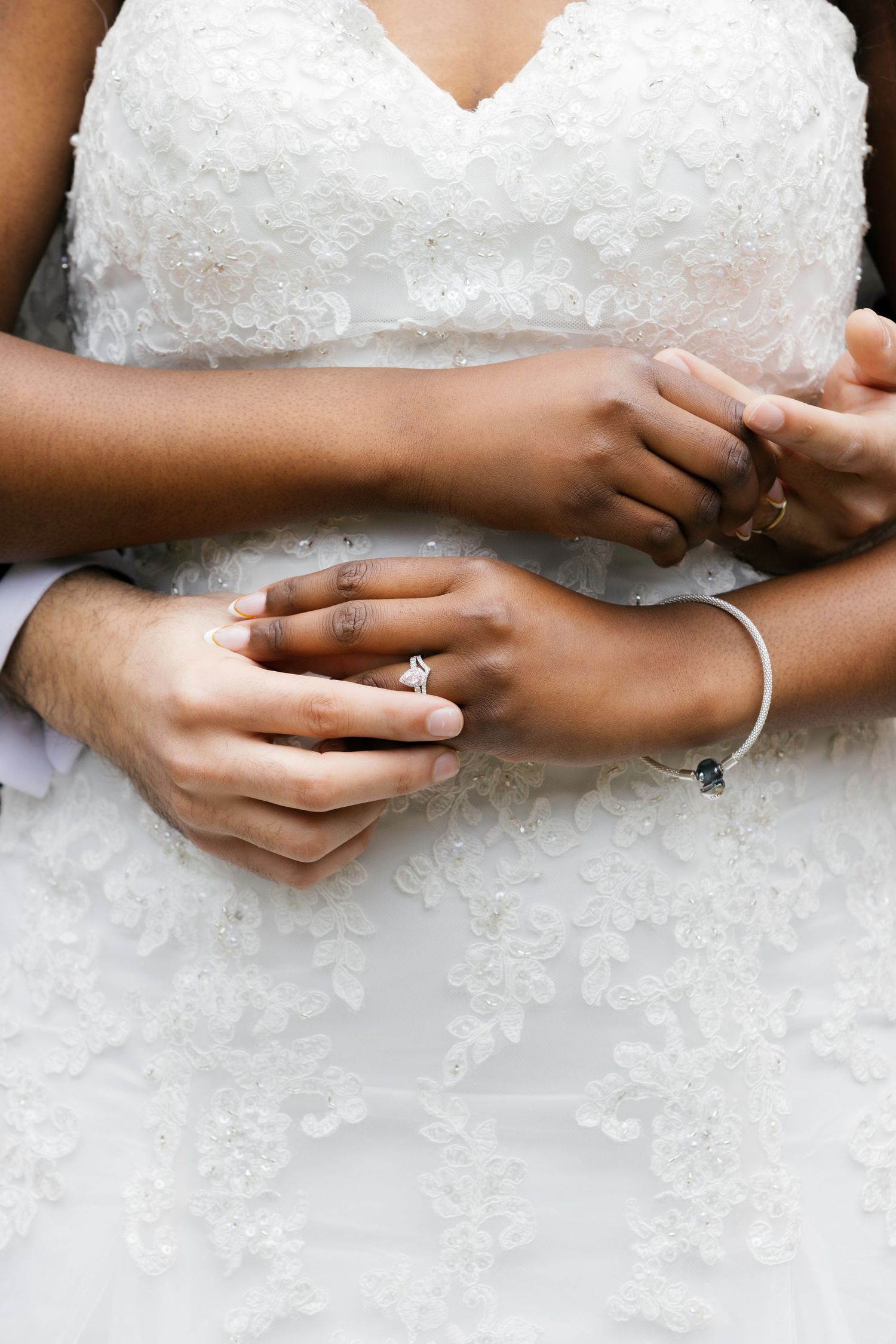 Close-up of interracial couple's hands at wedding, bride wearing diamond engagement ring and silver bracelet.