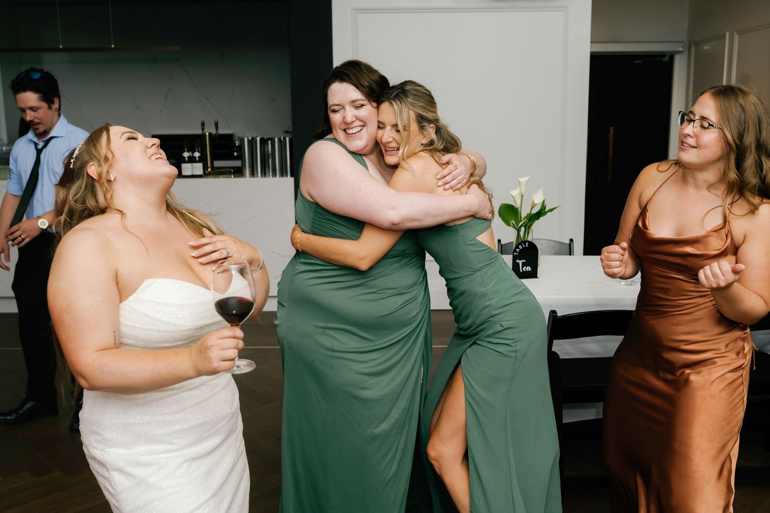 Wedding party in green and brown dresses celebrating together at reception.