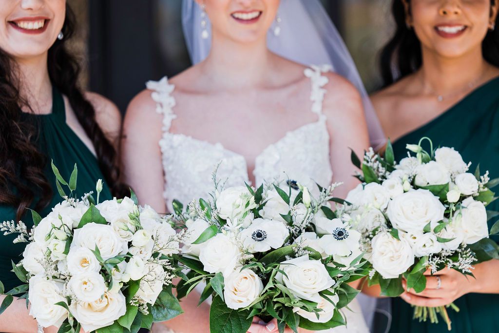 Bridesmaids in matching navy blue dresses hold elegant white and green floral bouquets at a wedding celebration.