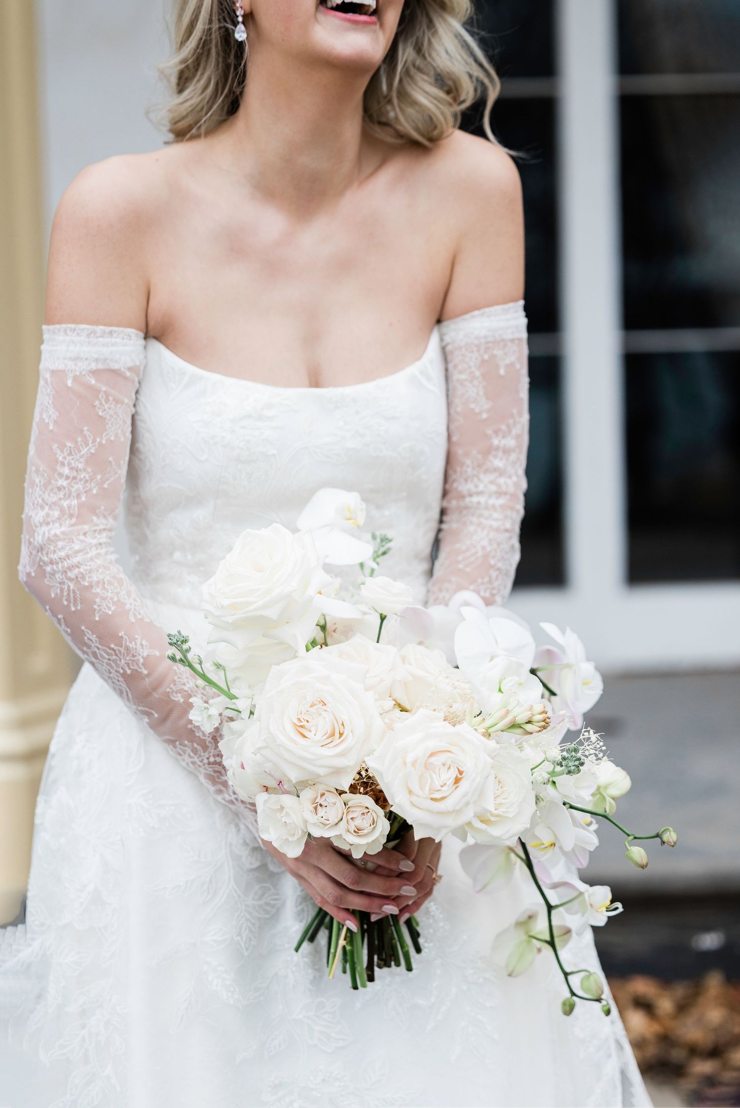 Elegant off-shoulder lace wedding dress with white floral bouquet.