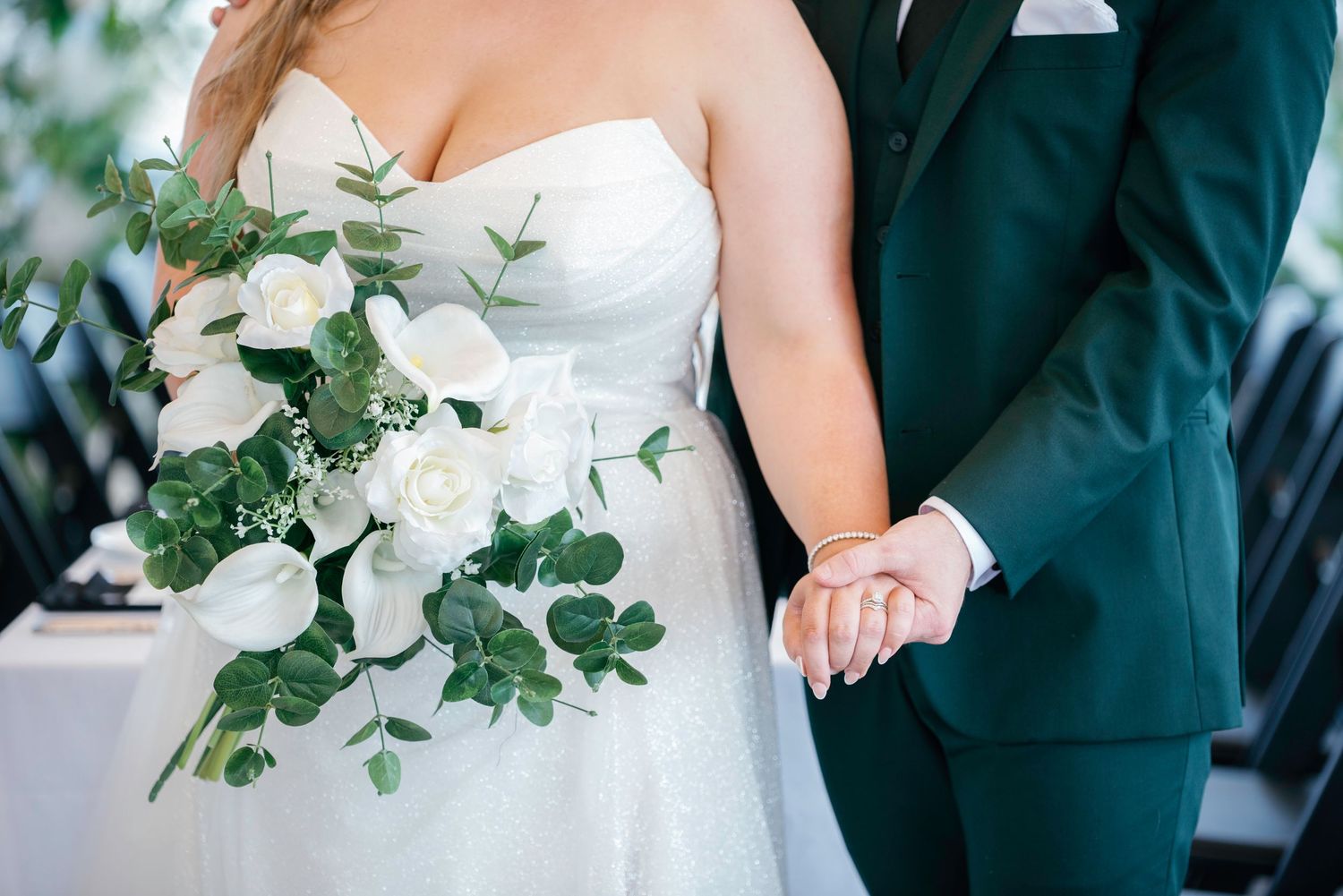 Wedding couple poses with elegant white floral bouquet and greenery.