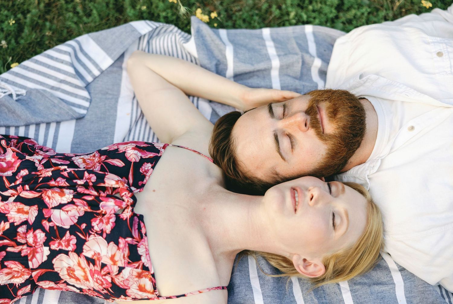 Couple lying together on a striped blanket outdoors.