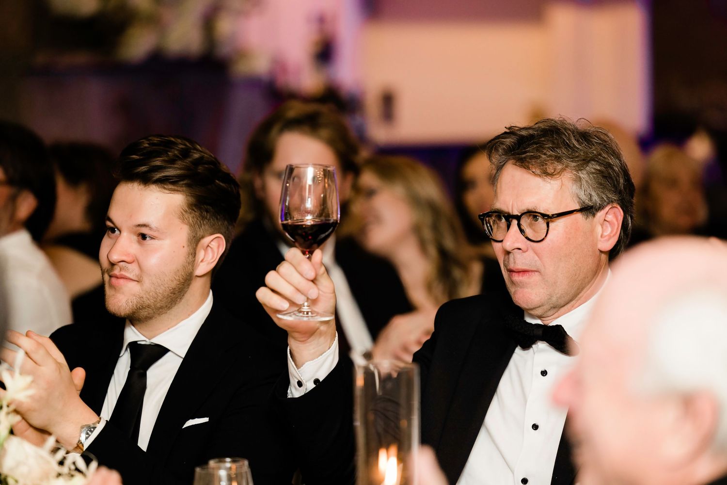 Wedding guests in formal attire seated at reception dinner tables.