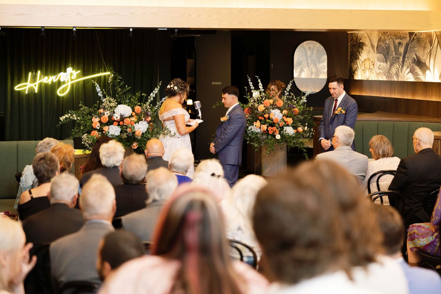 Indoor wedding ceremony with couple at altar, floral arrangements, and seated guests in an elegant venue.