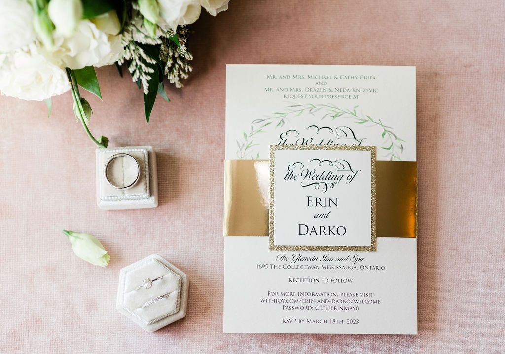 Wedding invitation suite with white flowers, calligraphy, and elegant stationery on a blush pink background.