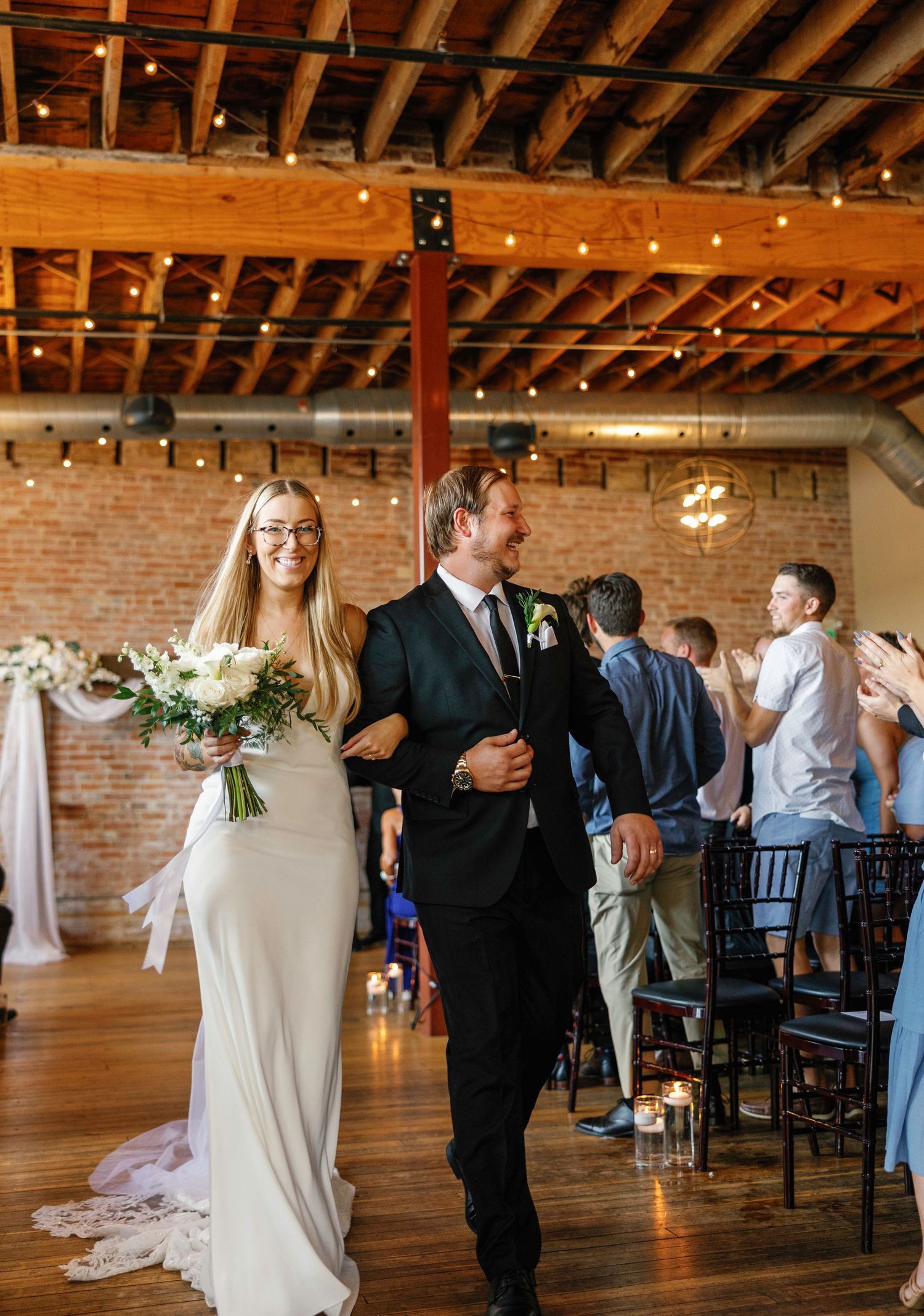 Elegant indoor wedding reception venue with brick walls, wooden ceiling beams, and white drapery decorations.