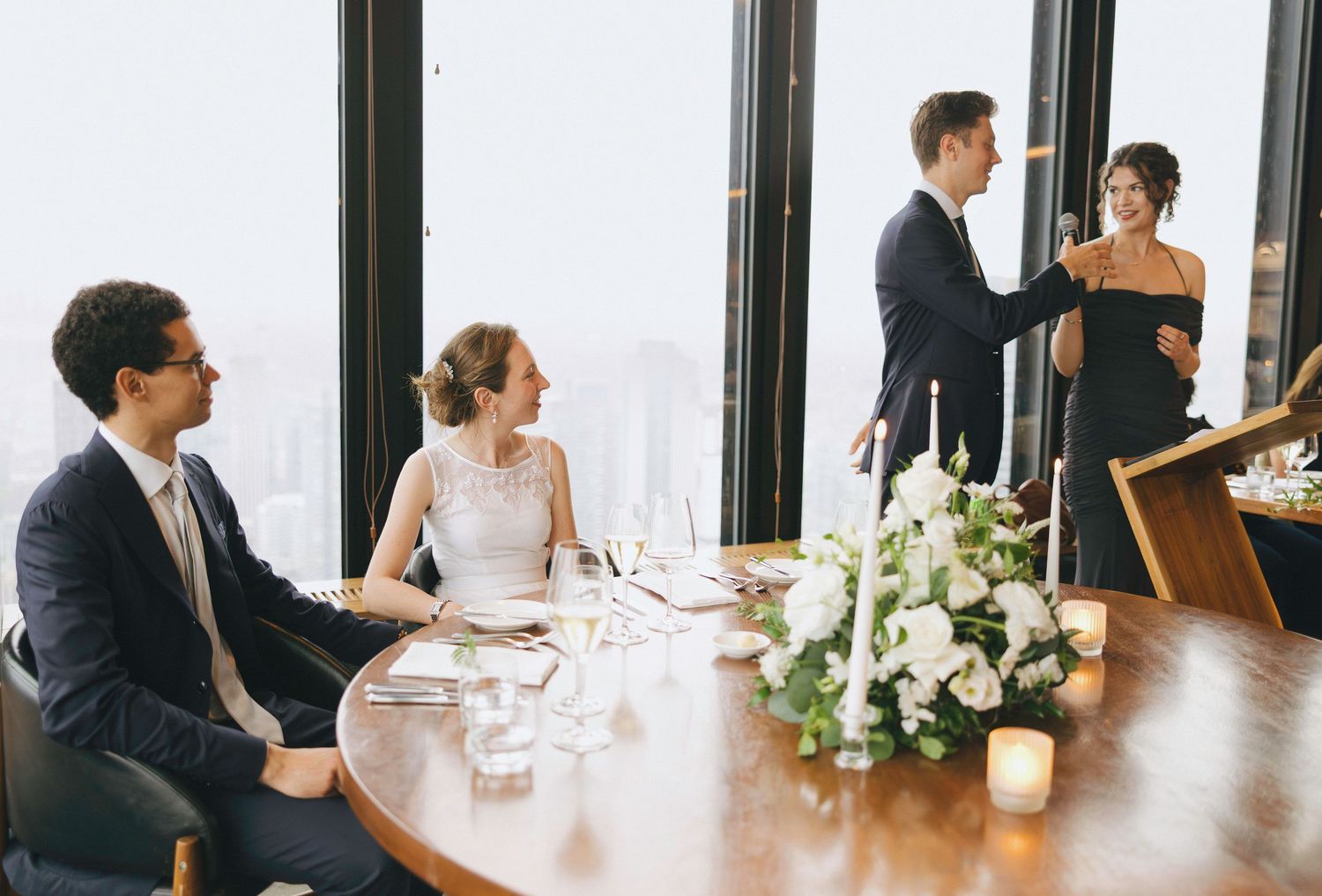 Elegant dining setup with white floral arrangements and place settings along a window-lit table.