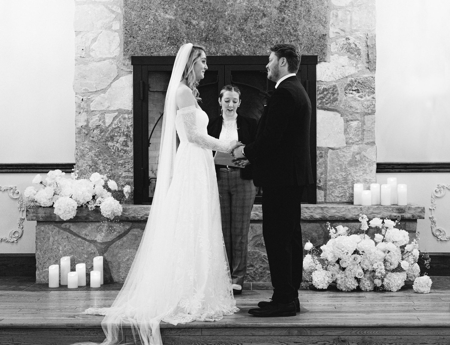 Wedding ceremony taking place in elegant stone-walled venue with candle decorations.