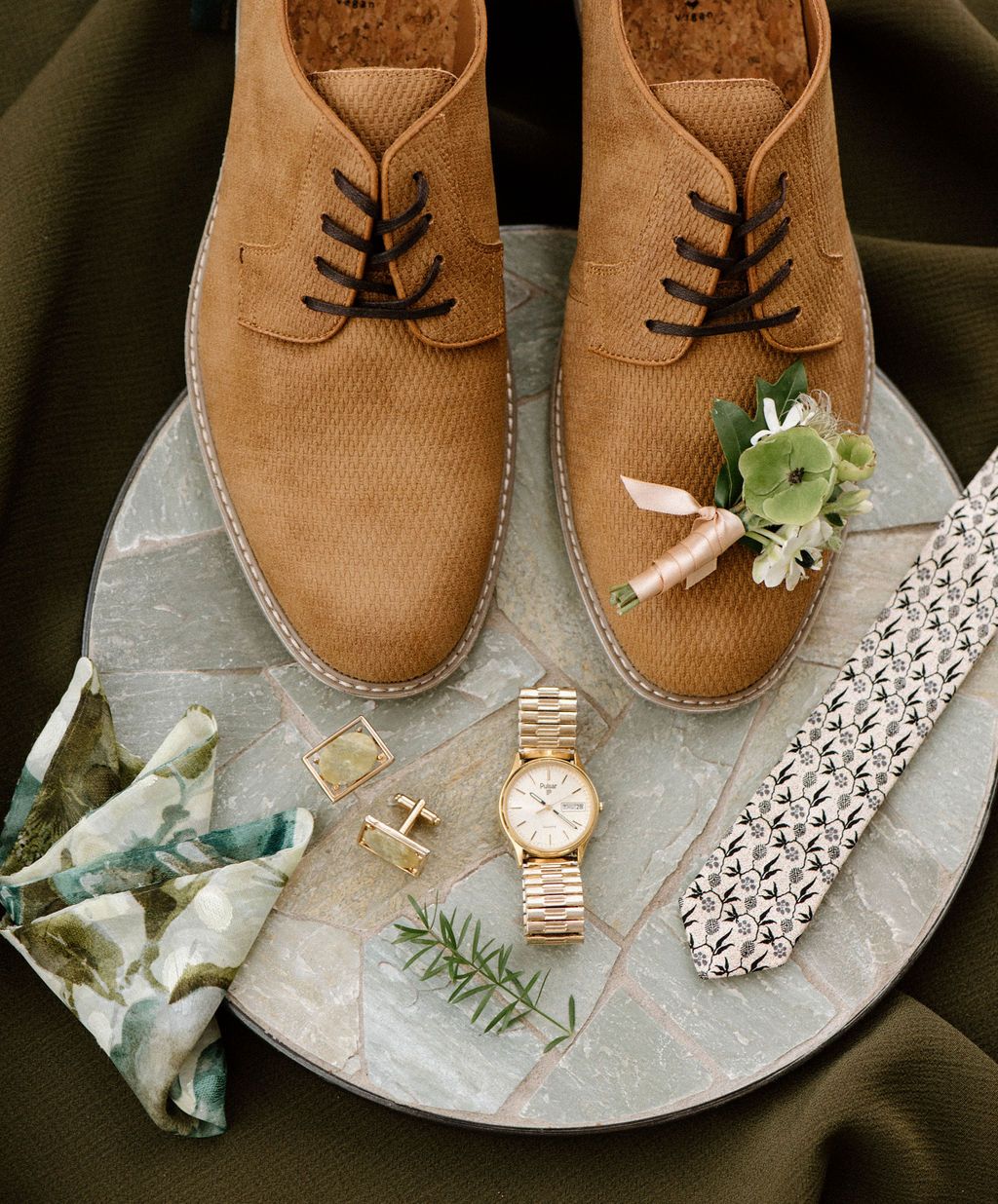 Styled wedding detail shot of brown leather shoes with watch and floral accessories.