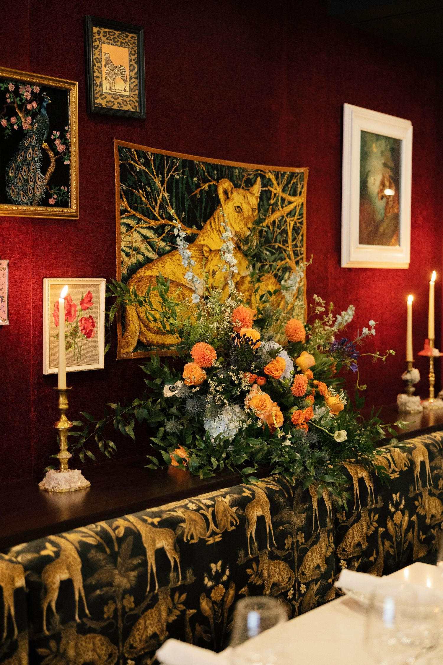 Elegant wedding reception with floral centerpiece, tapestry wall art, and candlelight on deep red walls.