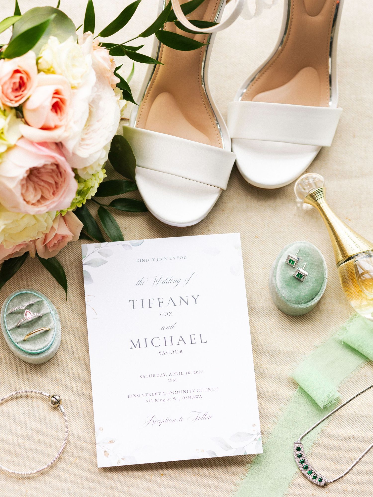 Elegant wedding flat lay with white heels, floral bouquet, invitation for Tiffany and Michael, rings, and Dior perfume.