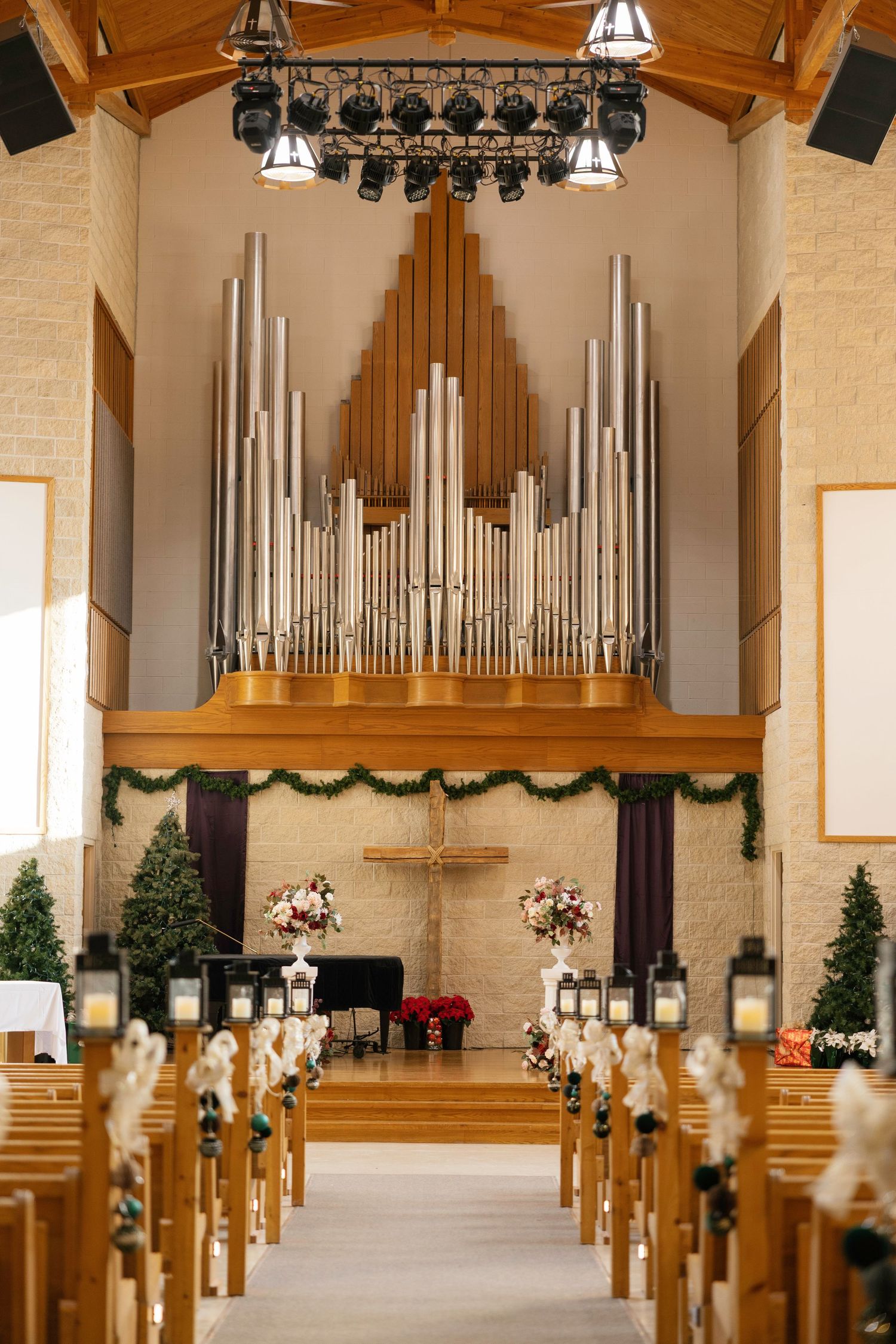 Church interior with pipe organ, wooden pews, cross altar, and Christmas decorations including garlands and poinsettias.