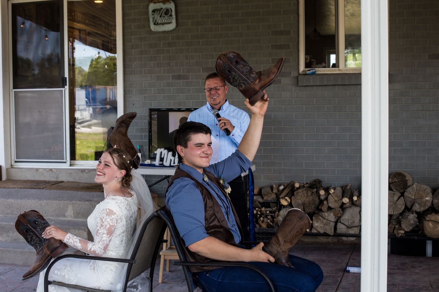 Bride and groom sitting on porch chairs as man raises cowboy hat behind them.